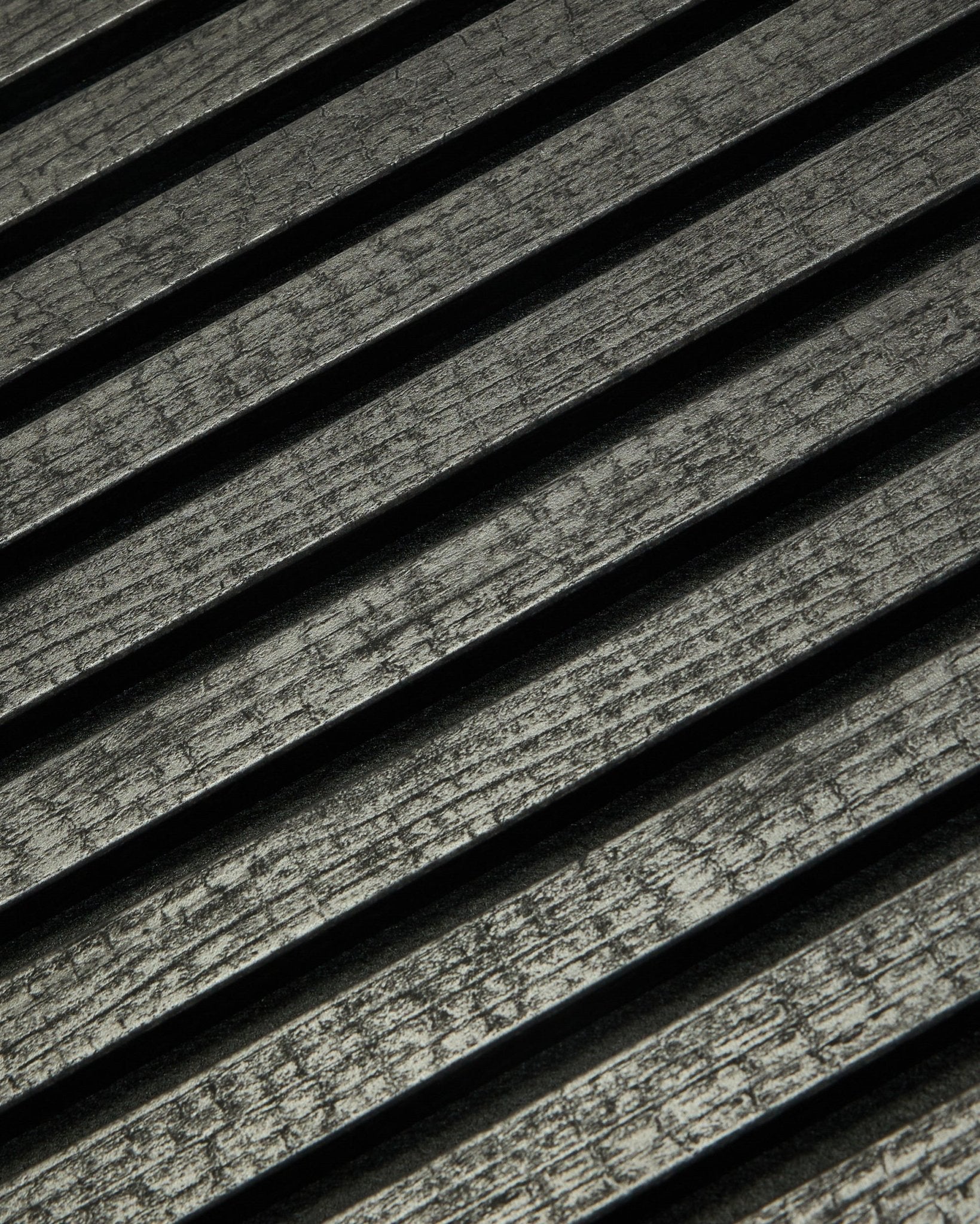 Nærbilde av WoodUpp Rebel Akupanel i Charcoal (240x60 cm) som viser black, rillete akustiske spiler arrangert diagonalt for bedre lydabsorpsjon.