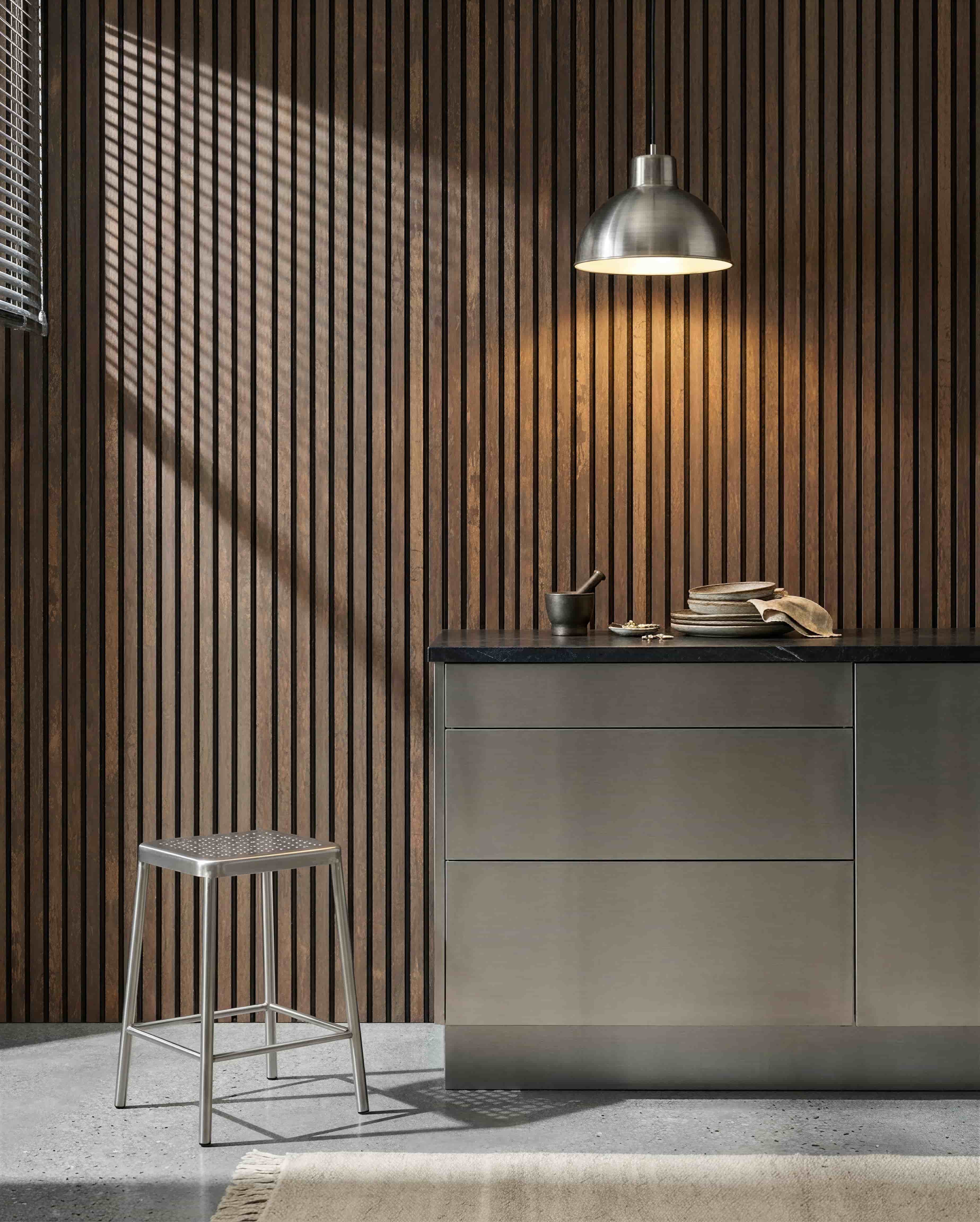 Kjøkken med en WoodUpp Akupanel Oxide Copper akustisk spilevegg, benkeplate i rustfritt stål, metallkrakk, pendellampe, diverse servise og morter og støter.