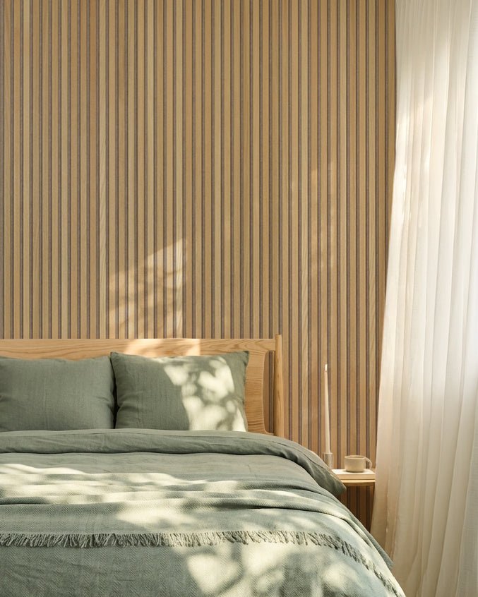 Minimalistisk nordisk soverom med en WoodUpp Akupanel eikevegg Akustikkpanel, sengetøy i salviegrønt, sengeramme i tre og lette hvite gardiner.