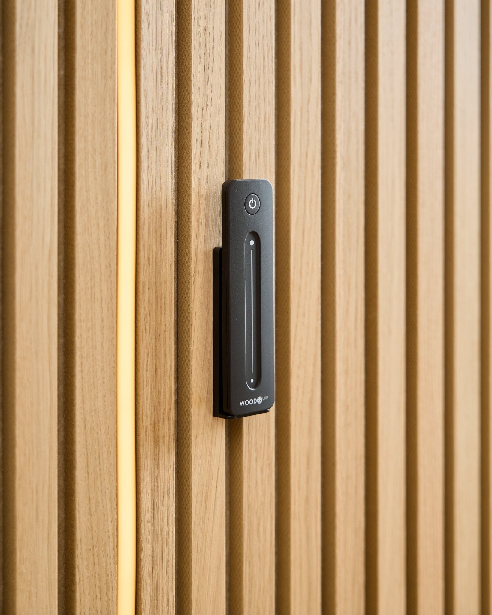 En WoodUpp Lumi | Remote / LED Striplight er montert på et lyst trepanel Akustikkpanel, med en gul kabel synlig bak trespilene.