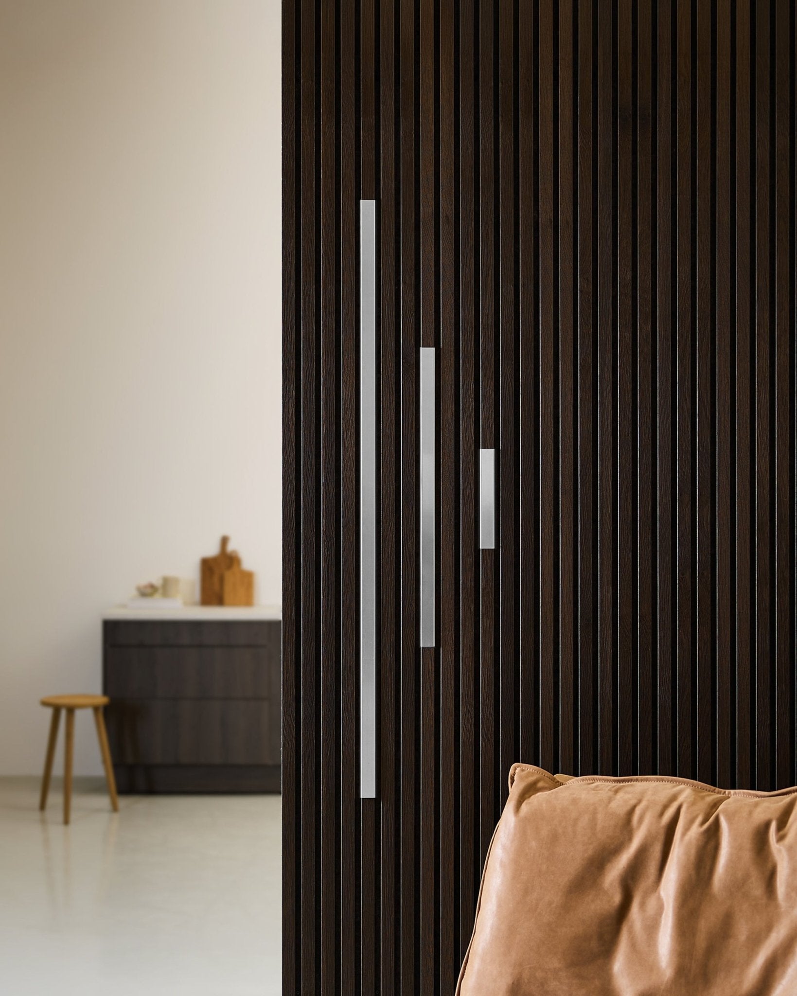 Minimalistisk interiør med en Akustikkpanel-vegg i mørkt tre, Liva Cover fra WoodUpp i polert steel (20 cm), en lysebrun pute og moderne møbler.