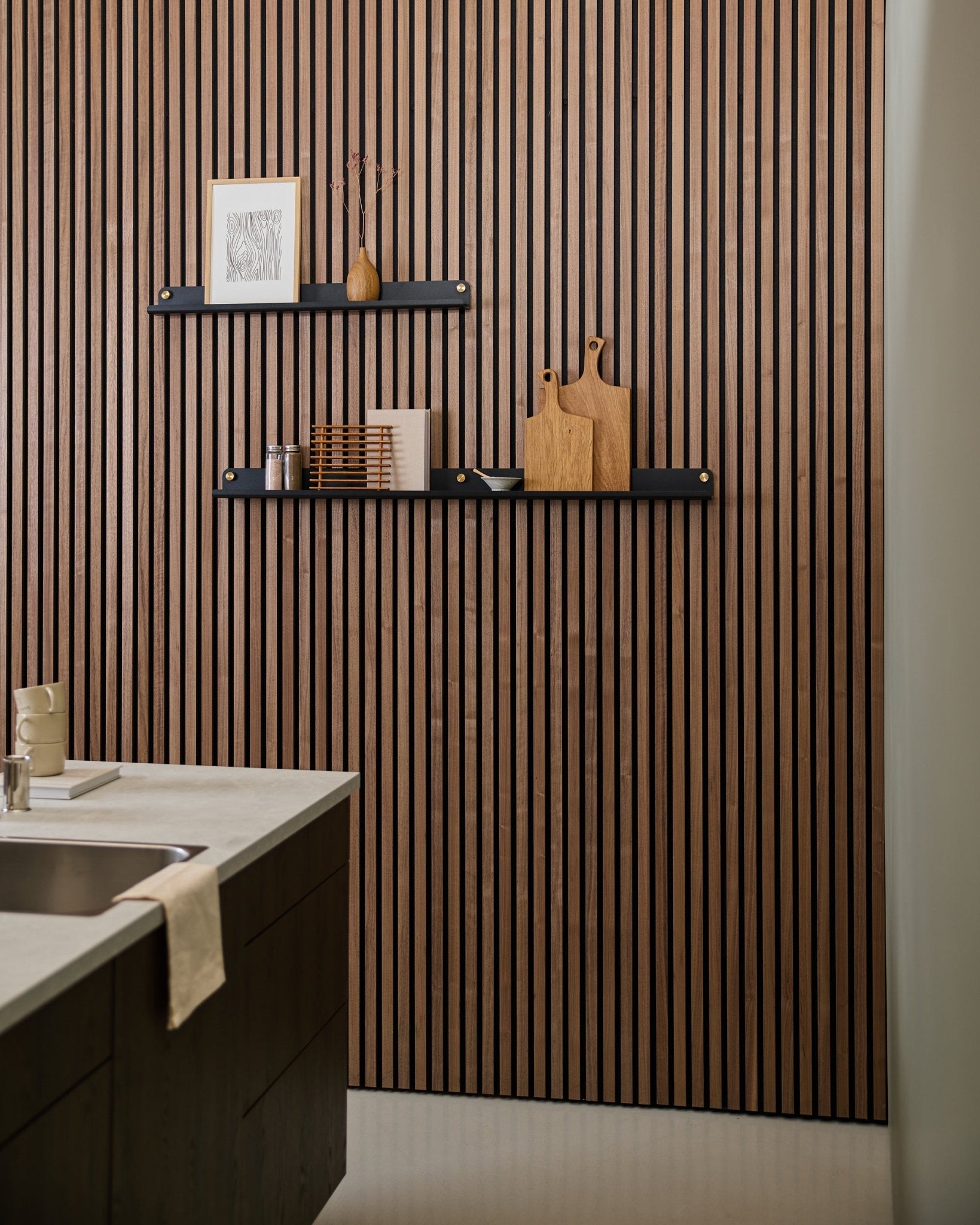 Moderne kjøkken med et akustisk spilepanel i nordisk stil, en black WoodUpp Norr smal hylle (115,9 cm) til dekor, og et håndkle drapert over vasken.