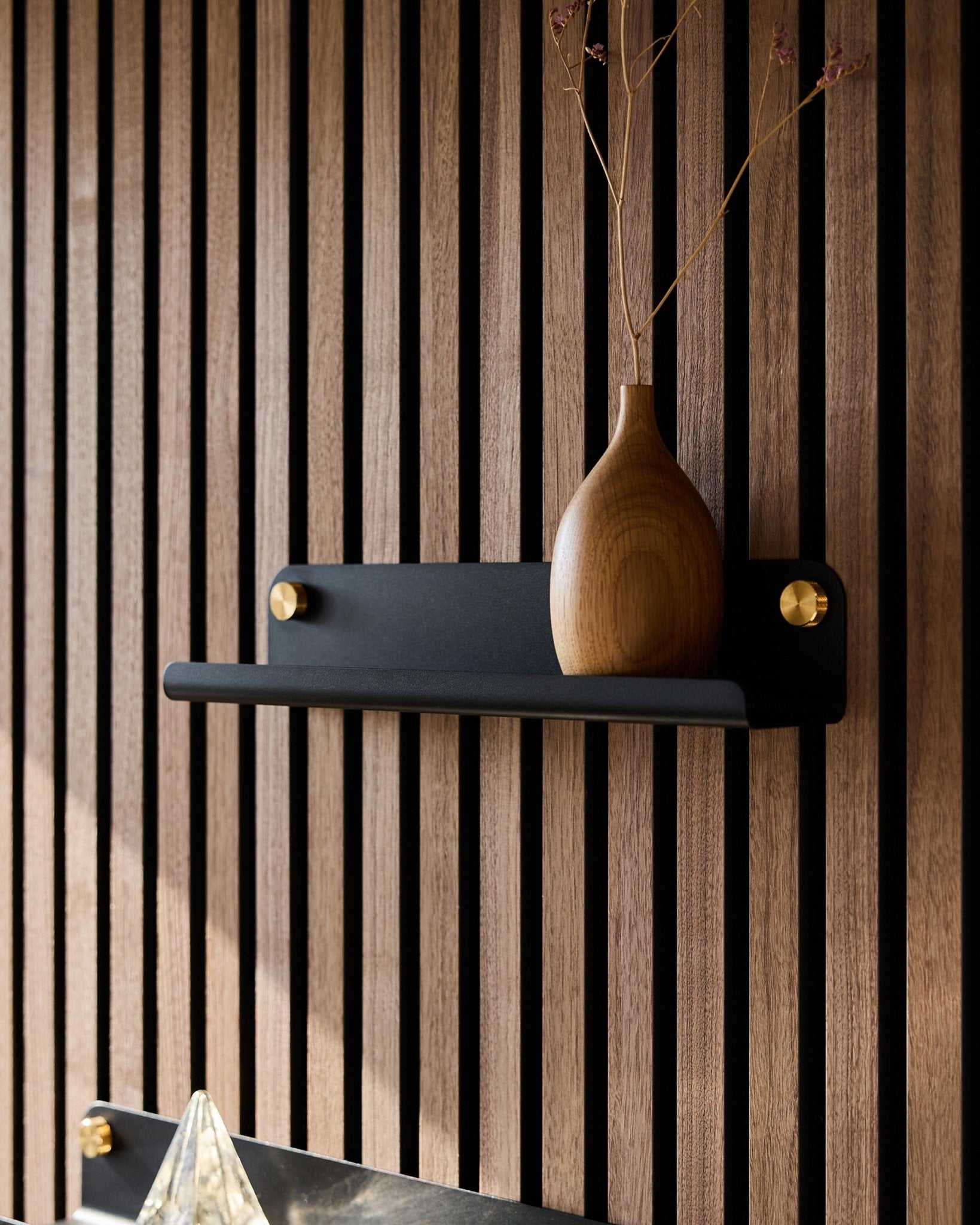 En vase i tre med tørkede grener på en black WoodUpp Norr smal hylle (35,9 cm), plassert foran et vertical akustikkpanel med spiler i nordisk stil.