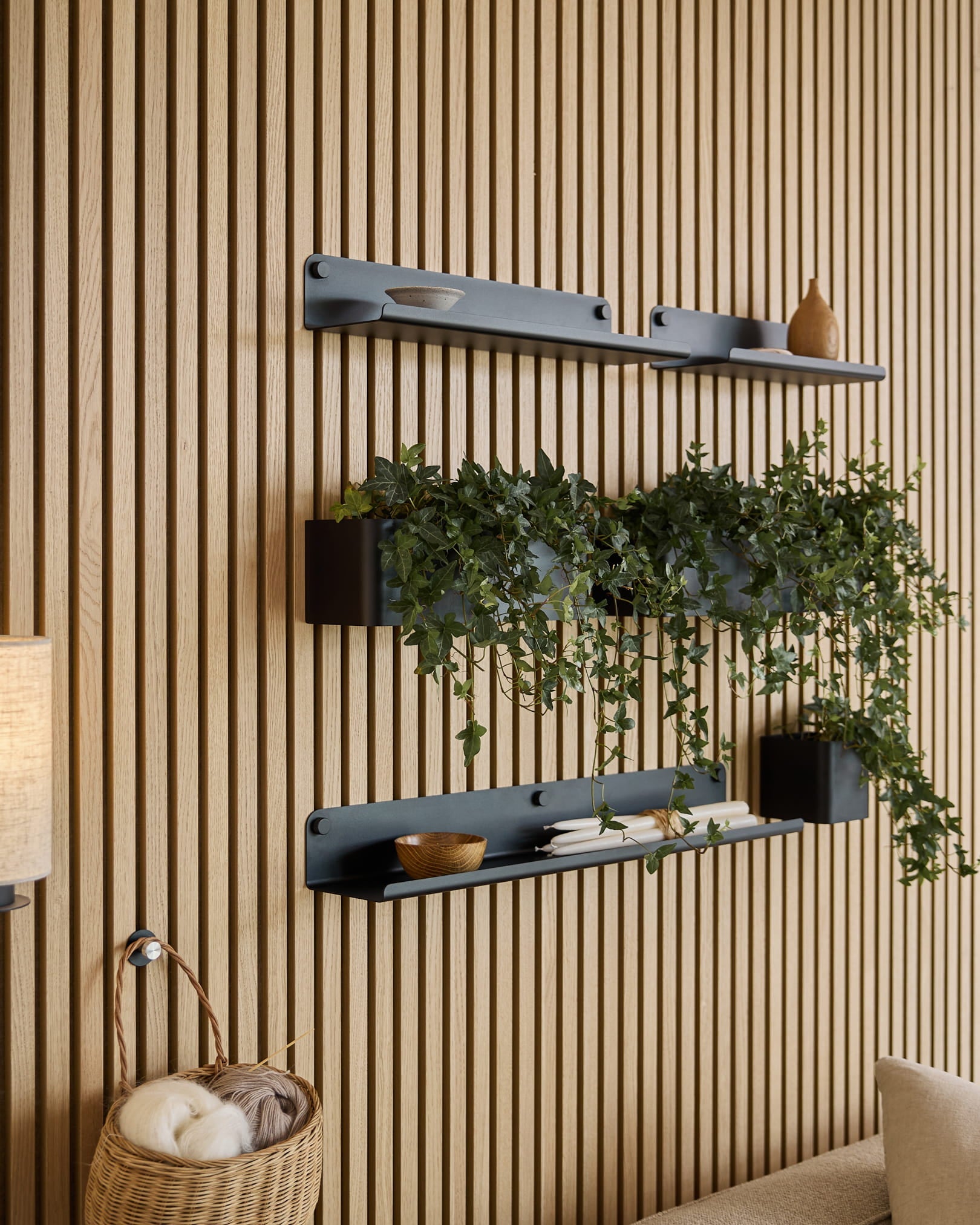 Tre black Norr | Plant Box hyller fra WoodUpp med dekor og en plante er montert over en flettet kurv med garn, foran et grønt akustisk spileveggpanel.