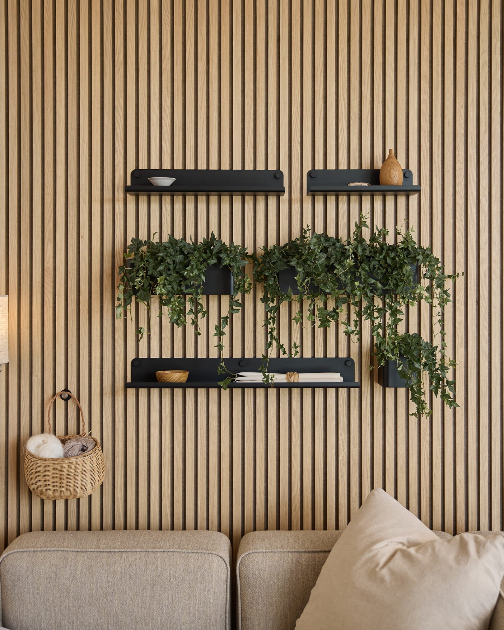 En moderne stue med et nordisk akustisk spileveggpanel, black hyller, hengende planter i WoodUpps Norr Plant Box (35,9 cm, Black) og en beige sofa.