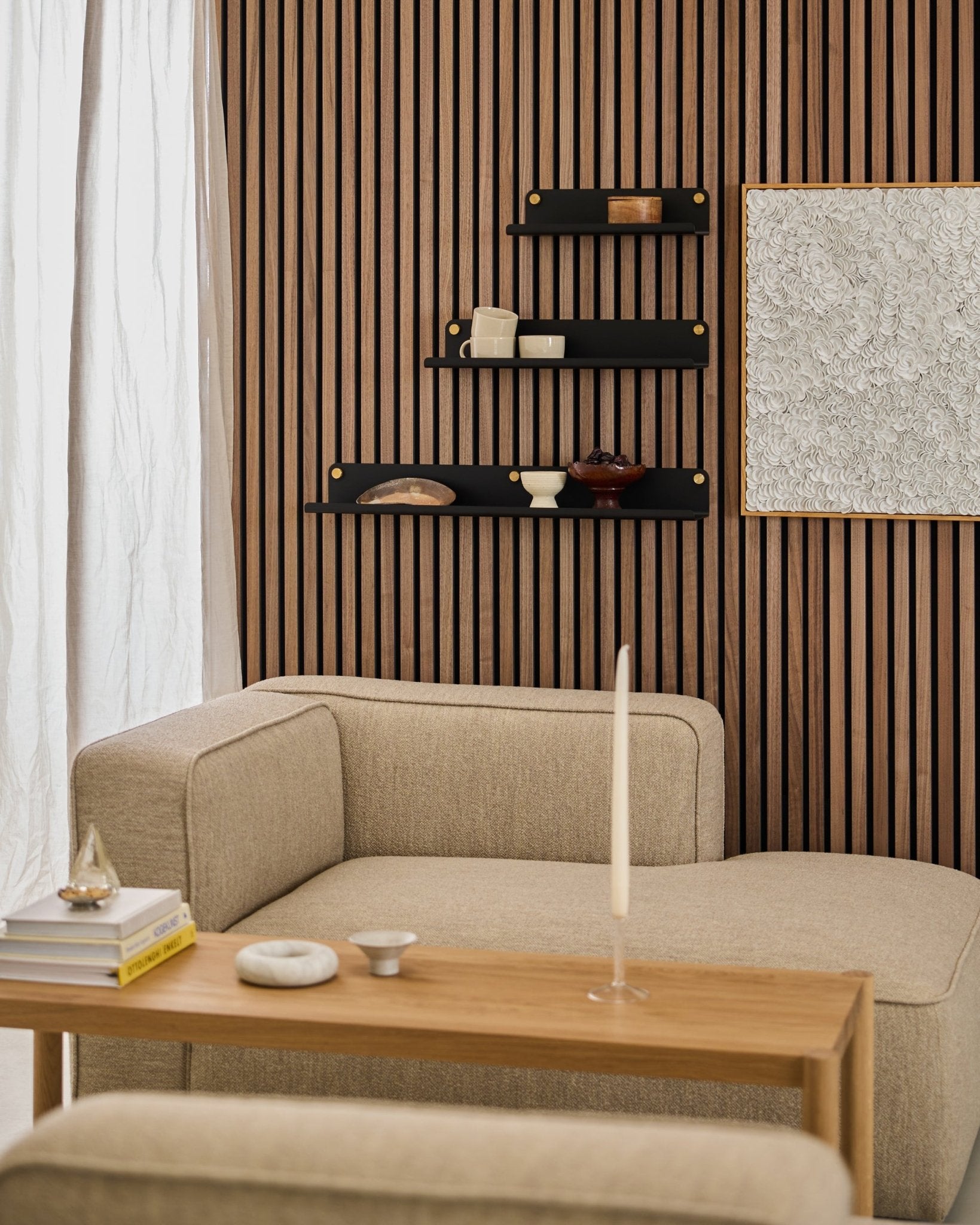 Moderne stue med en beige sofa, trebord, black WoodUpp Norr Wide Shelf (51,9 cm), og en teksturert Akupanel Akustikkpanel vegg med abstrakt kunst.