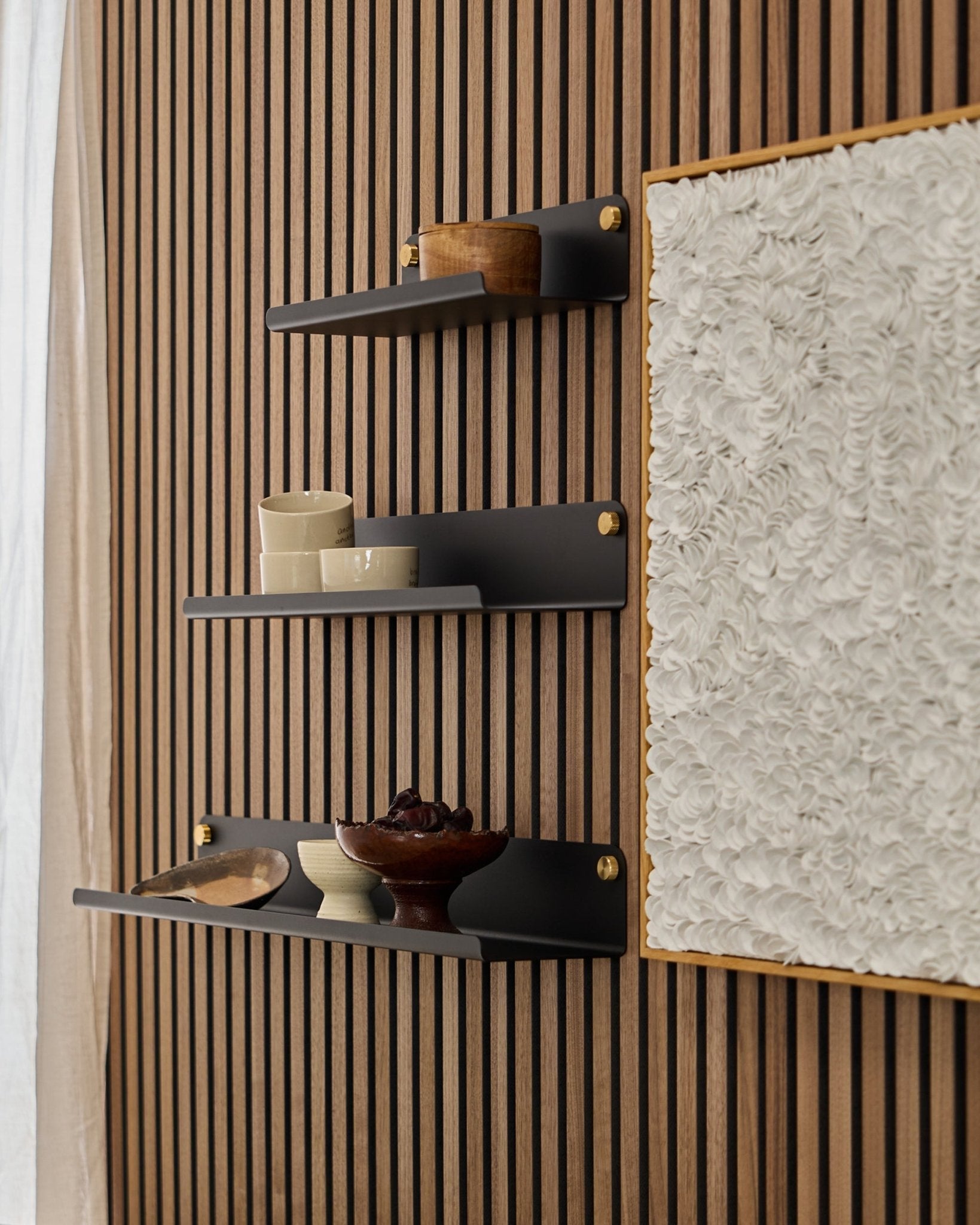 Tre black WoodUpp Norr Wide Shelf (51,9 cm) montert på et WoodUpp Akupanel akustisk trepanel, ved siden av teksturert hvit kunst, med skåler og beholdere i tre.