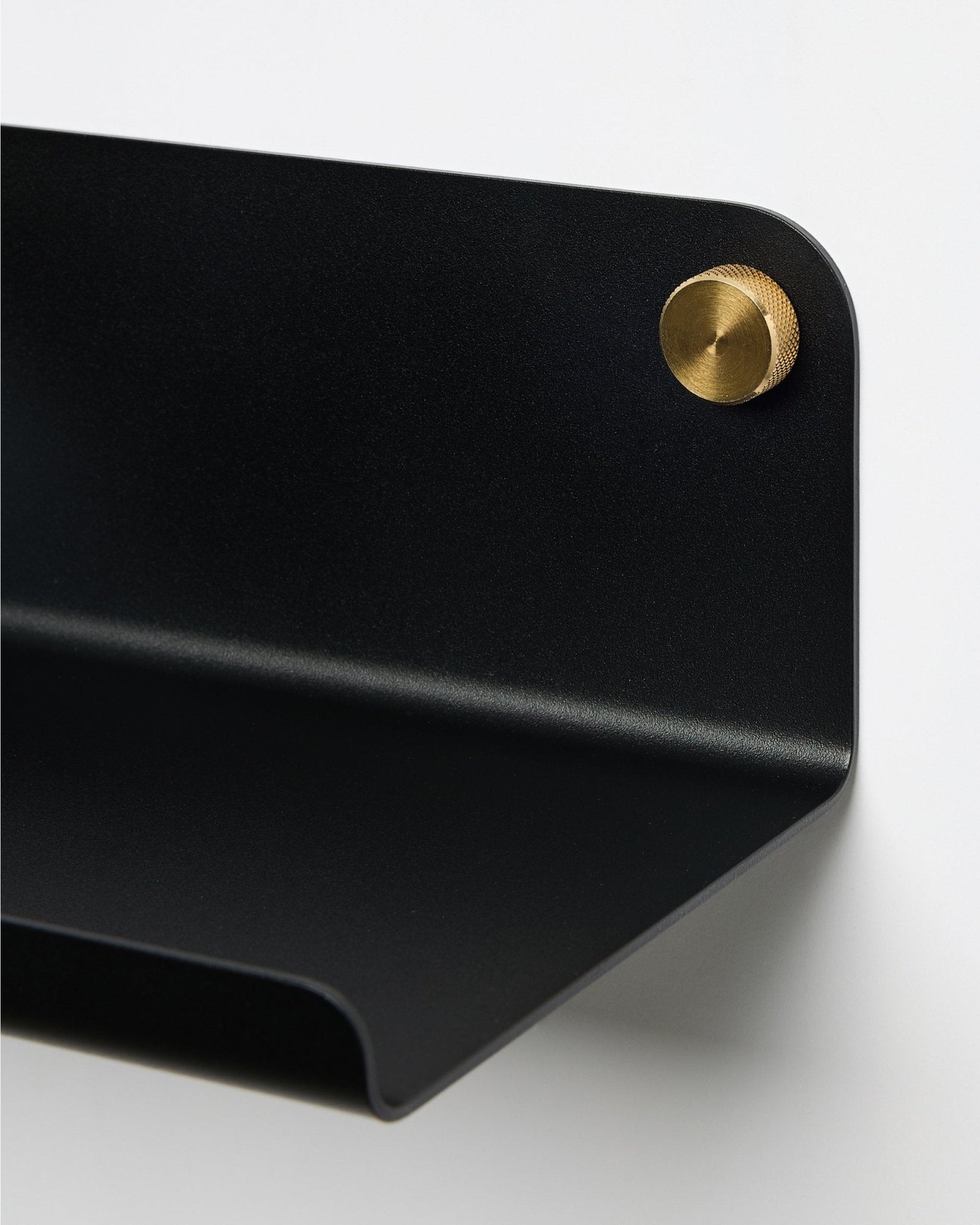 Nærbilde av WoodUpp Norr Wide Shelf i black, 35,9 cm, med en buet kant, festet til veggen med en rund brass skrue. Nordisk minimalistisk design.