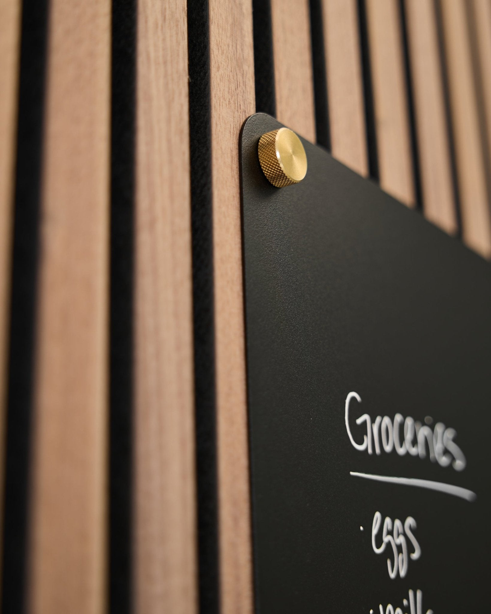 En black tavle med en håndskrevet handleliste er montert på et WoodUpp akustisk spilepanel med to M5x10 mm brass fingerskruer.