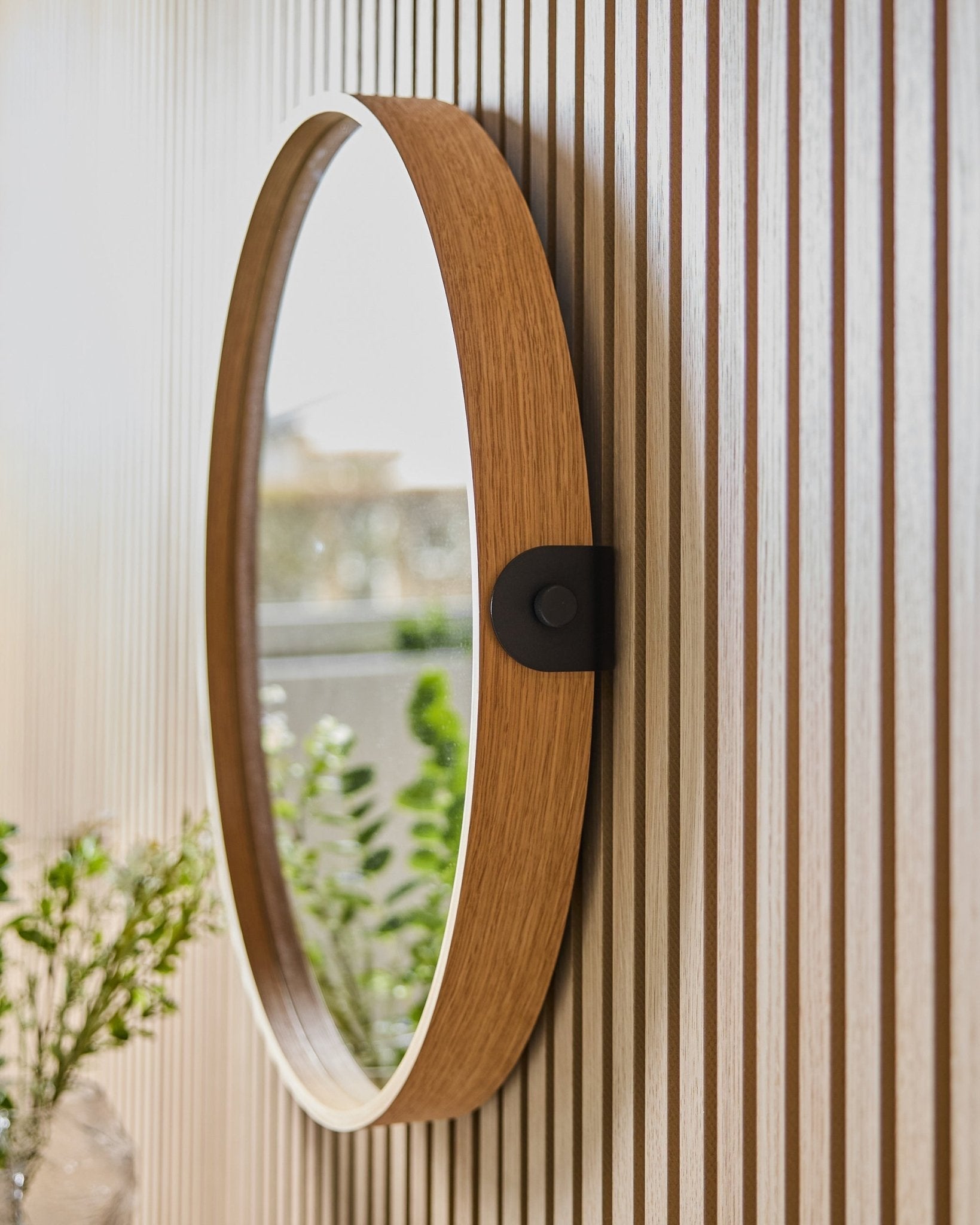 Linn | Mirror / Natural Oak fra WoodUpp montert på en stripet Akustikkpanel-vegg, som reflekterer grønt og naturlig lys fra et nærliggende vindu.