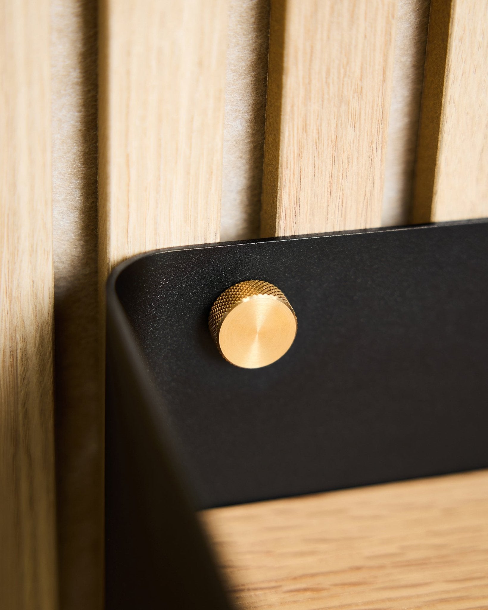 Nærbilde av to brass WoodUpp Fingerskruer (M5x10 mm, 20x8,8), festet til en black brakett montert på en lys nordisk treoverflate Akustikkpanel.