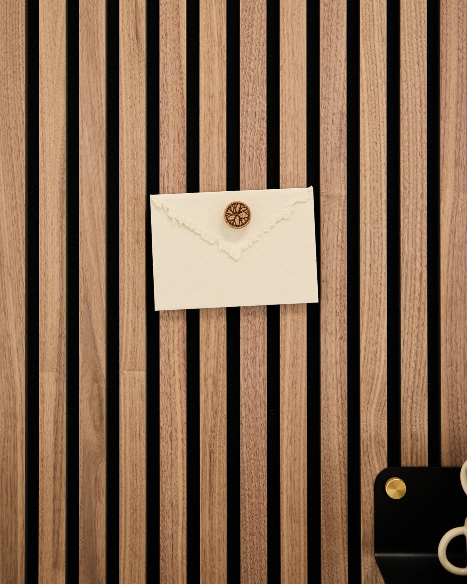En kremfarget konvolutt med vokssegl er festet til et akustisk spilepanel i eik fra WoodUpp med Norr Poster Magnet-settet i Natural Oak; saks og brett står i nærheten.