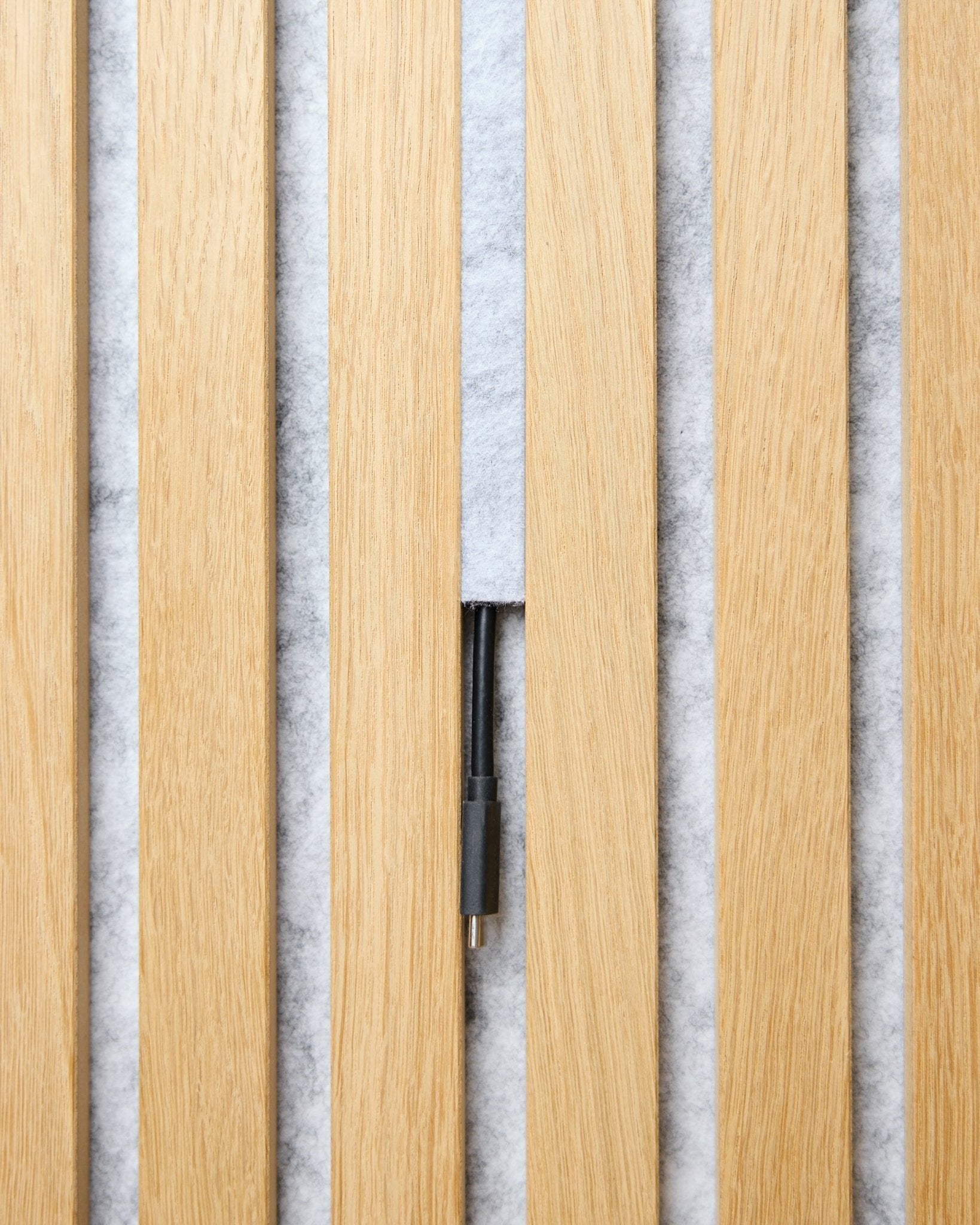 Dupps Pop-on Cable Cover-sett (grey, 3 stk.) fra WoodUpp organiserer kabler mellom lyse tre-Akupanel spiler på en hvit teksturert bakgrunn.