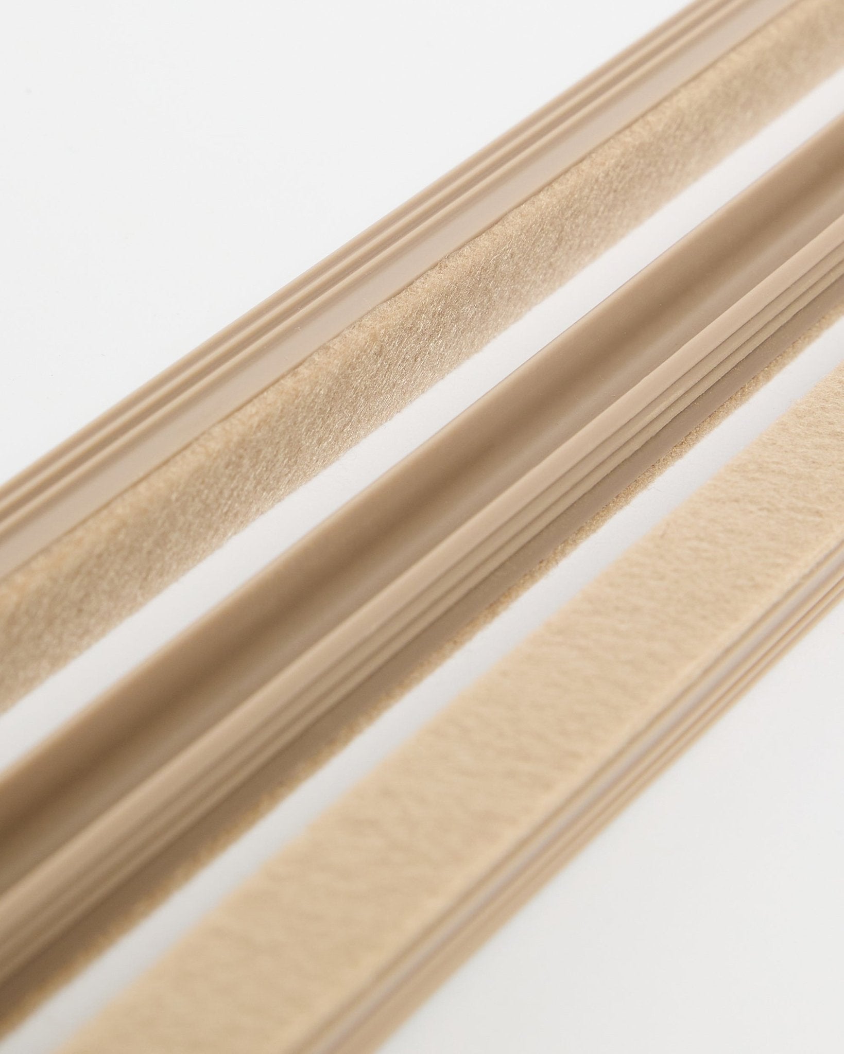 Beige WoodUpp Dupps Pop-on Cable Covers (3-pakning) med filttekstur og selvklebende bakside, vist på en hvit overflate for organisering av ledninger.