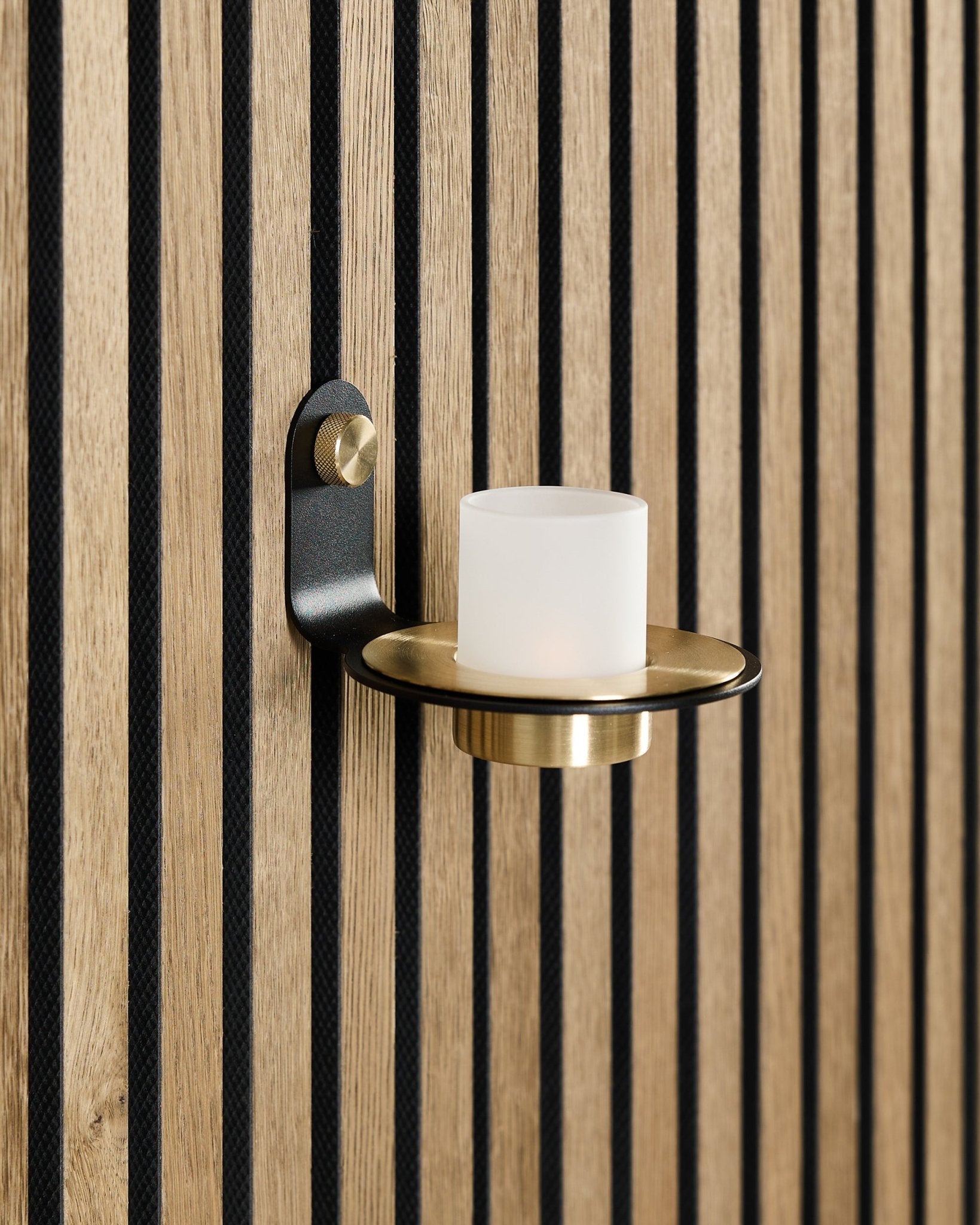 Norr Candle Holder i black og brass fra WoodUpp er montert på et nordisk Akupanel akustisk trepanel med vertical black spiler.
