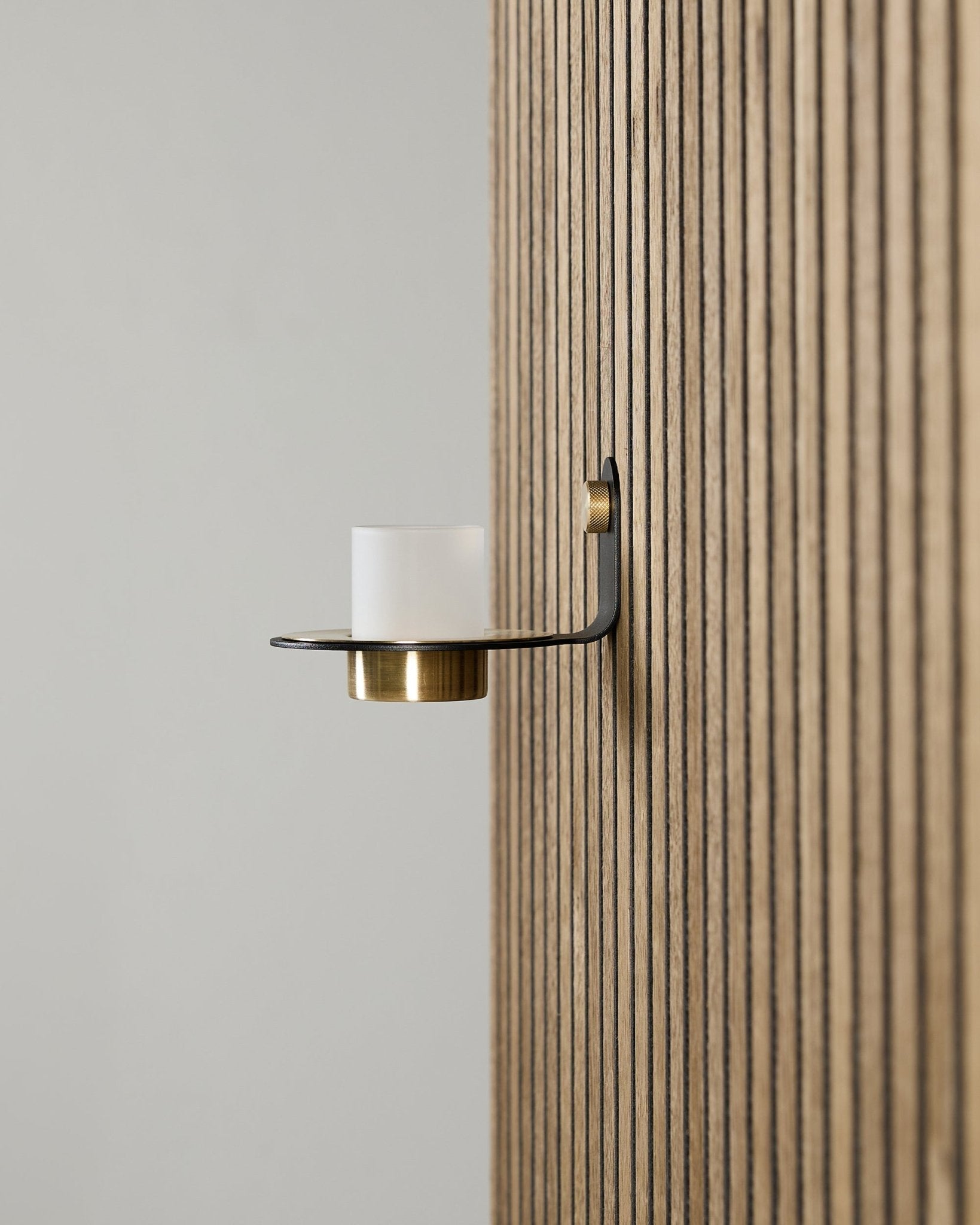 Norr Candle Holder i black og brass fra WoodUpp, montert på et vertical Akupanel Akustikkpanel, med frostet glass og brass detaljer.