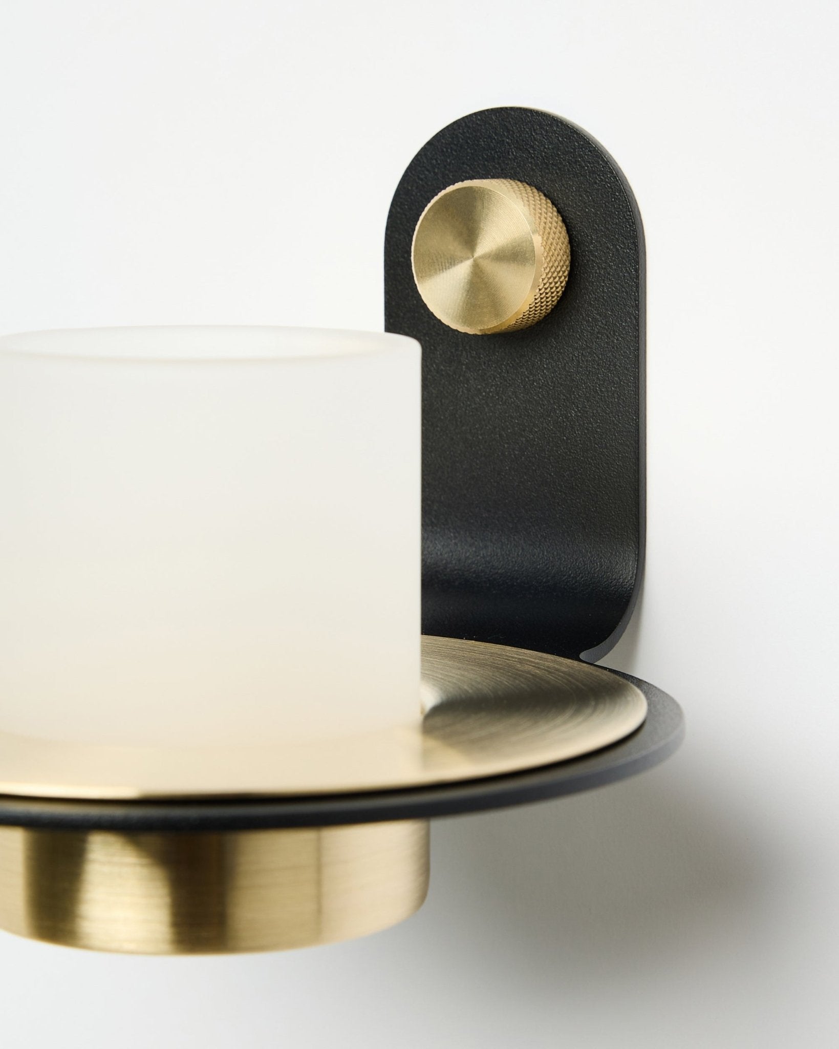 Norr Candle Holder fra WoodUpp, i black og brass, vist montert med LED-lys på et hvitt Akustikkpanel.