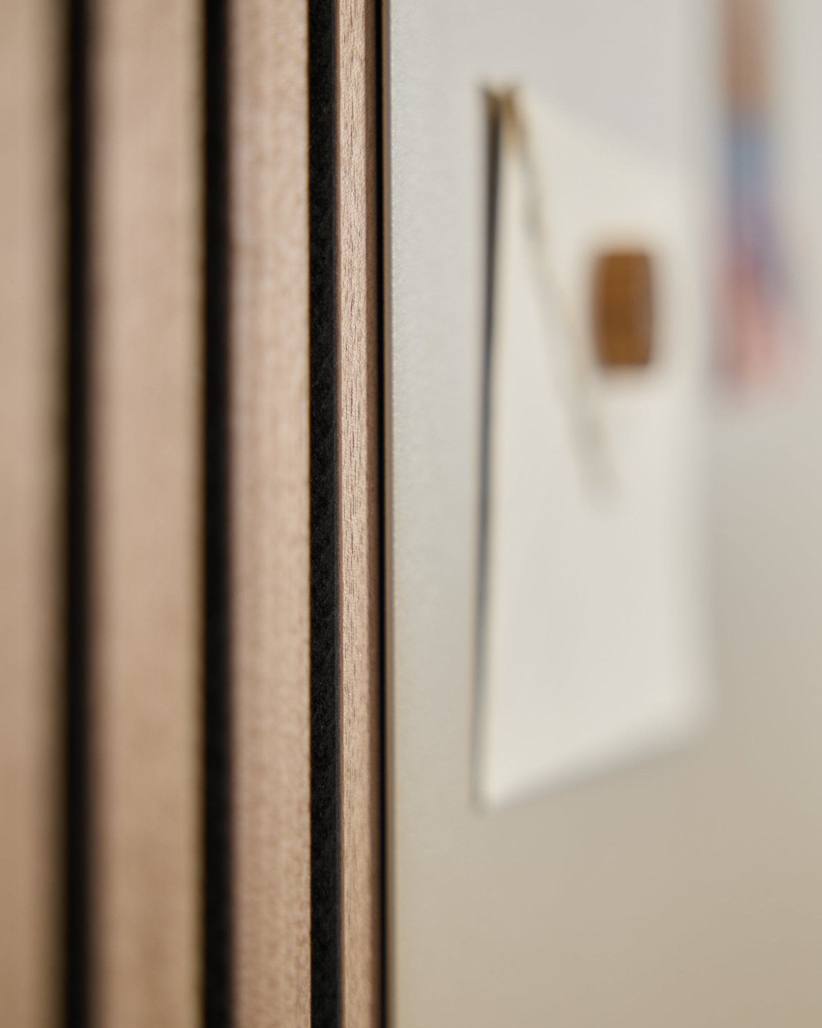 Nærbilde av et WoodUpp Akupanel akustisk trepanel med vertical spiler, ved siden av en uskarp large beige Norr magnettavle i bakgrunnen.