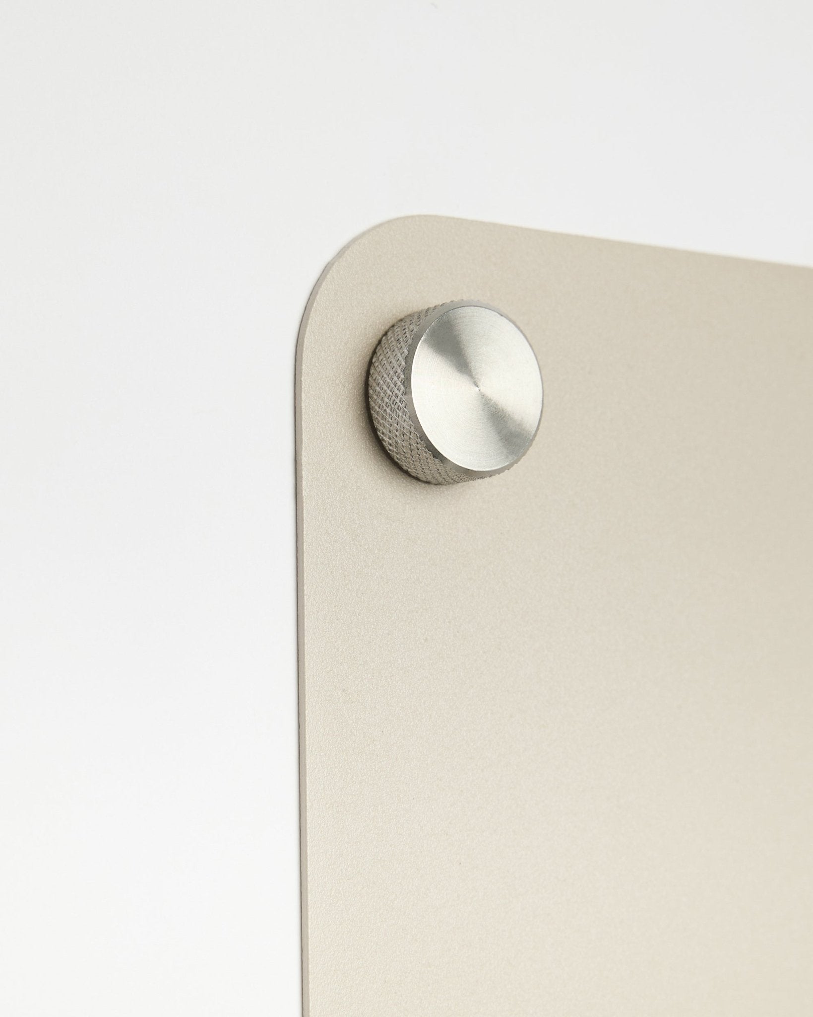 Nærbilde av et rundt knotttilbehør i metall festet til den large beige Norr magnettavlen fra WoodUpp, med detalj i frostet glass mot hvit bakgrunn.
