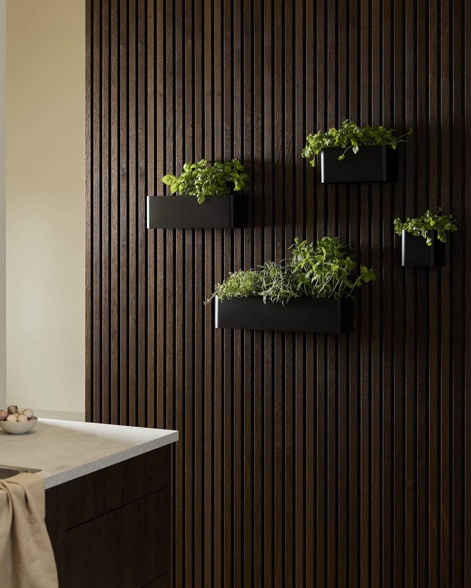 Black veggmonterte plantekasser og en WoodUpp Norr Plant Box med grønne urter på et mørkt trepanel Akupanel Akustikkpanel i et moderne kjøkken.