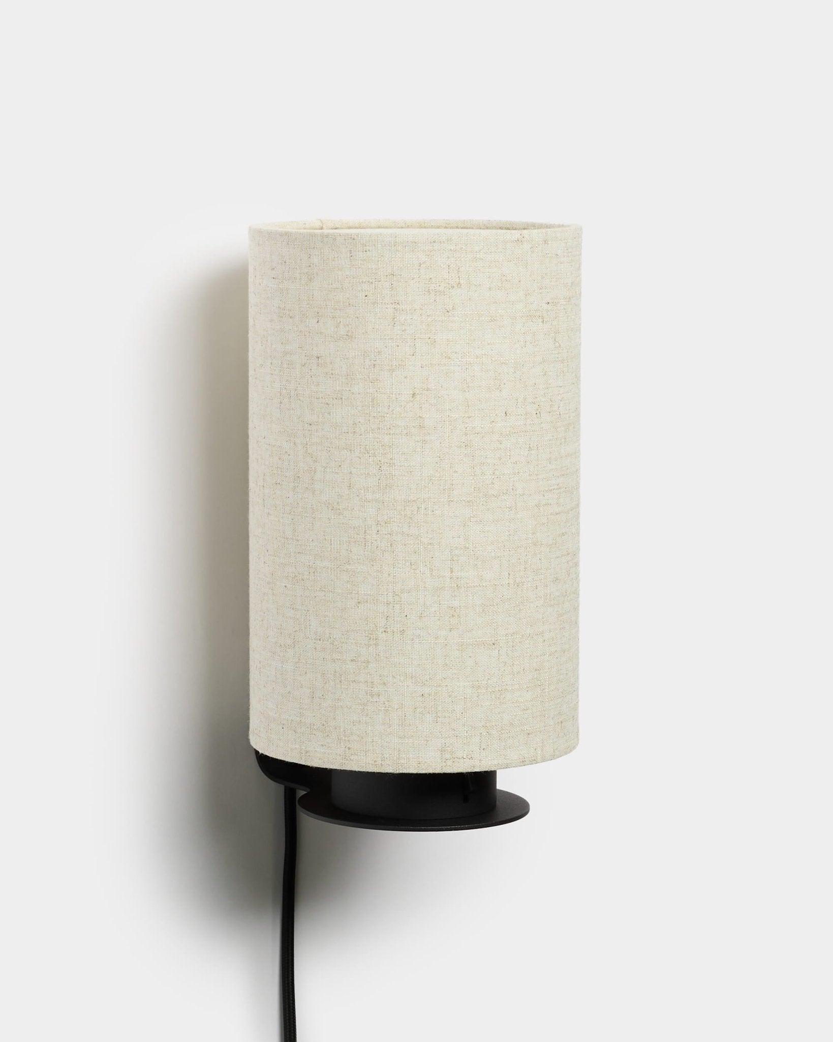 Feya vegglampe fra WoodUpp med metallfot i black, teksturert skjerm i lin-bomull i beige og synlig strømkabel i black. Nordisk minimalistisk design.