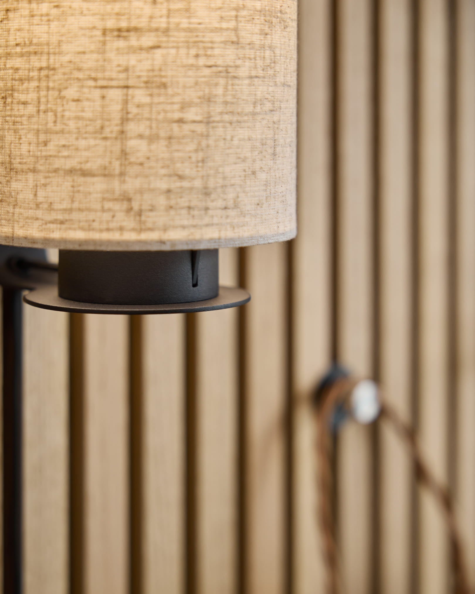 Feya vegglampe / Black/Beige fra WoodUpp med en skjerm i beige lin-bomull, metallfot i black og synlig kabel montert på et nordisk akustisk spilepanel.