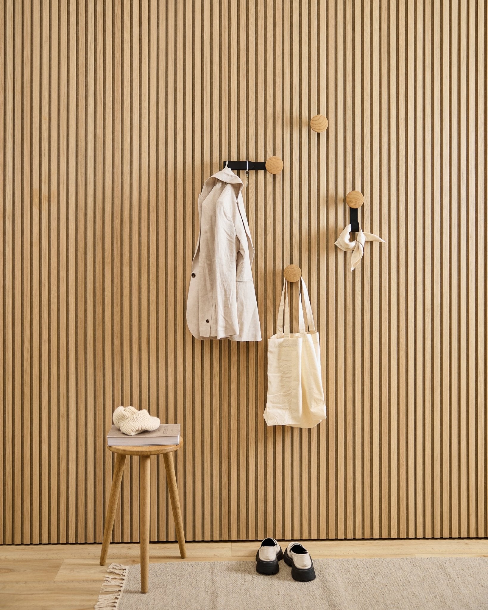 Minimalistisk entré med WoodUpp Linn Vertical Hanger i natural oak, med en beige frakk, handlenett, skjerf, krakk med tøfler og black-hvite sko.
