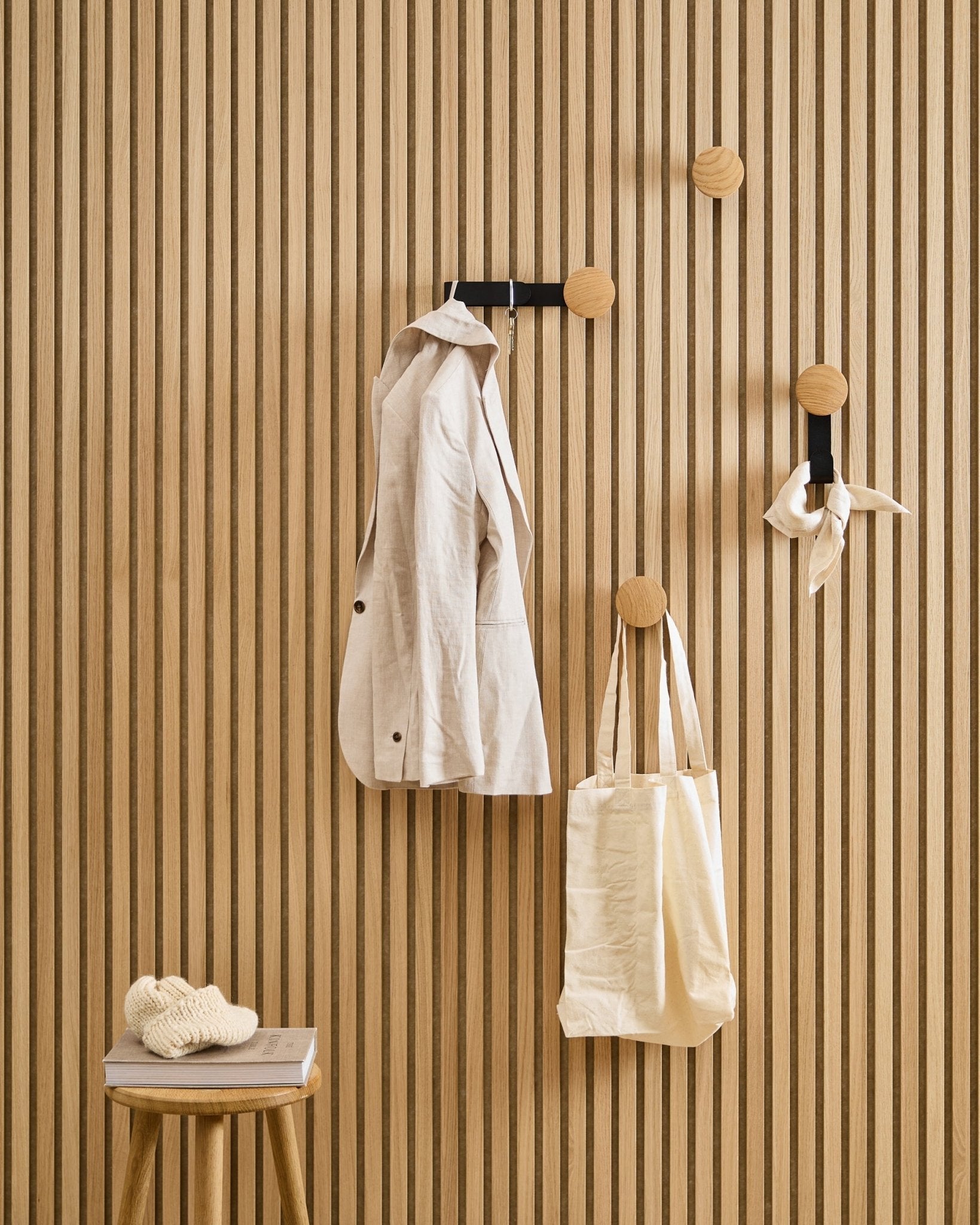 En beige jakke, handlenett og skjerf henger på WoodUpps Linn Horizontal Hanger i Natural Oak; en krakk ved siden av bærer en bok og et strikket plagg.