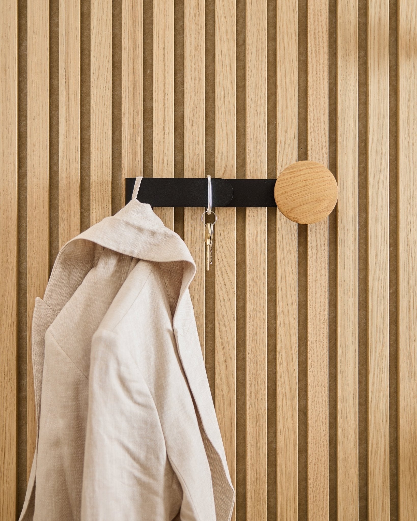En beige blazer og et nøkkelsett henger på WoodUpp Linn Horizontal Hanger i natural oak, montert på et natural oak Akupanel akustisk trepanel.