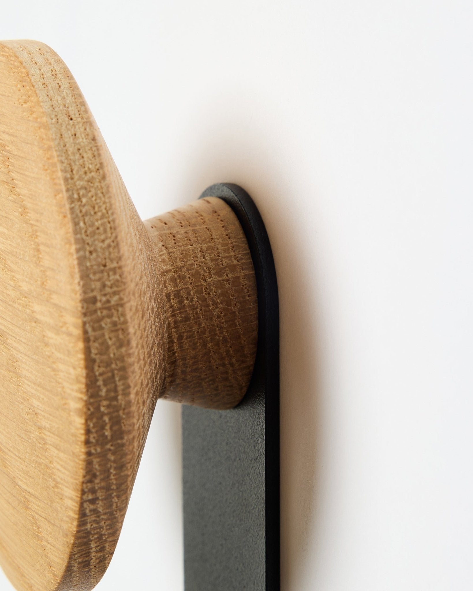 Nærbilde av Linn Vertical Hanger i natural oak fra WoodUpp, et rundt knaggtilbehør i tre montert på en black brakett, laget for Akupanel akustiske paneler.