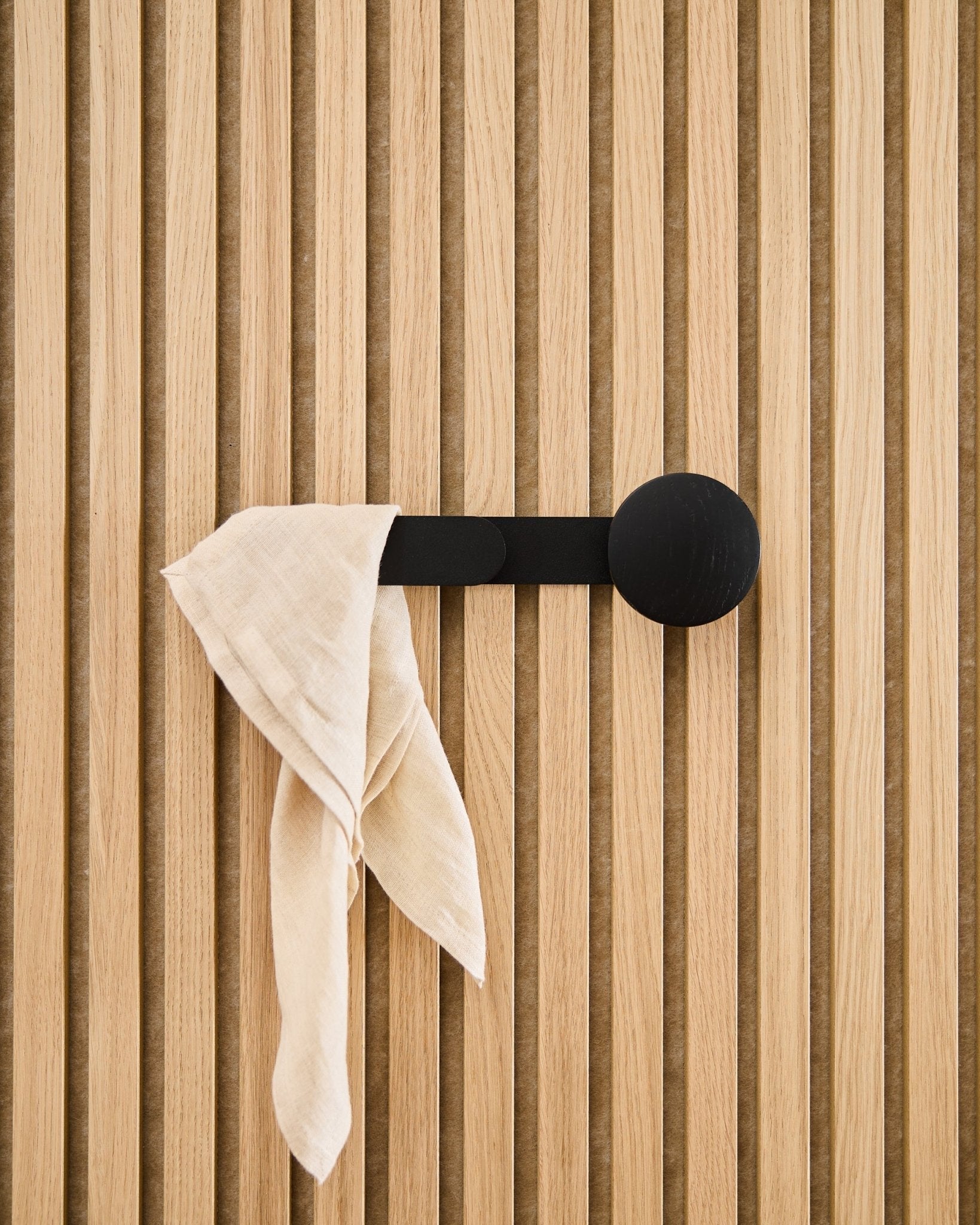Et beige tekstil henger over WoodUpp Linn Horizontal Hanger i Black Oak, festet til et vertical akustisk spilepanel.