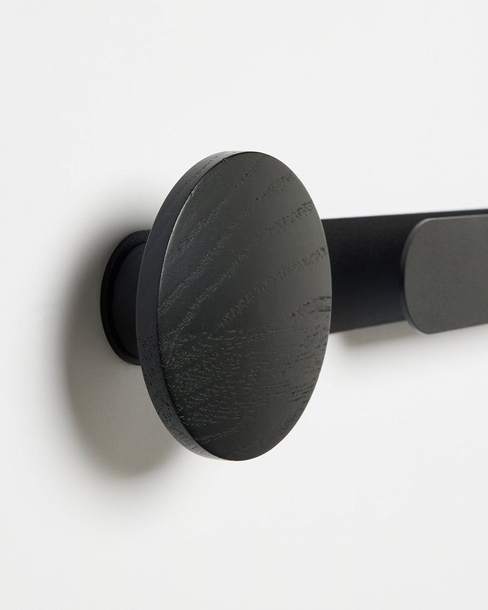 Nærbilde av WoodUpp Linn | Horizontal Hanger i Black Oak, med matt black finish, montert på en hvit vegg; tilbehør til akustiske trepaneler.