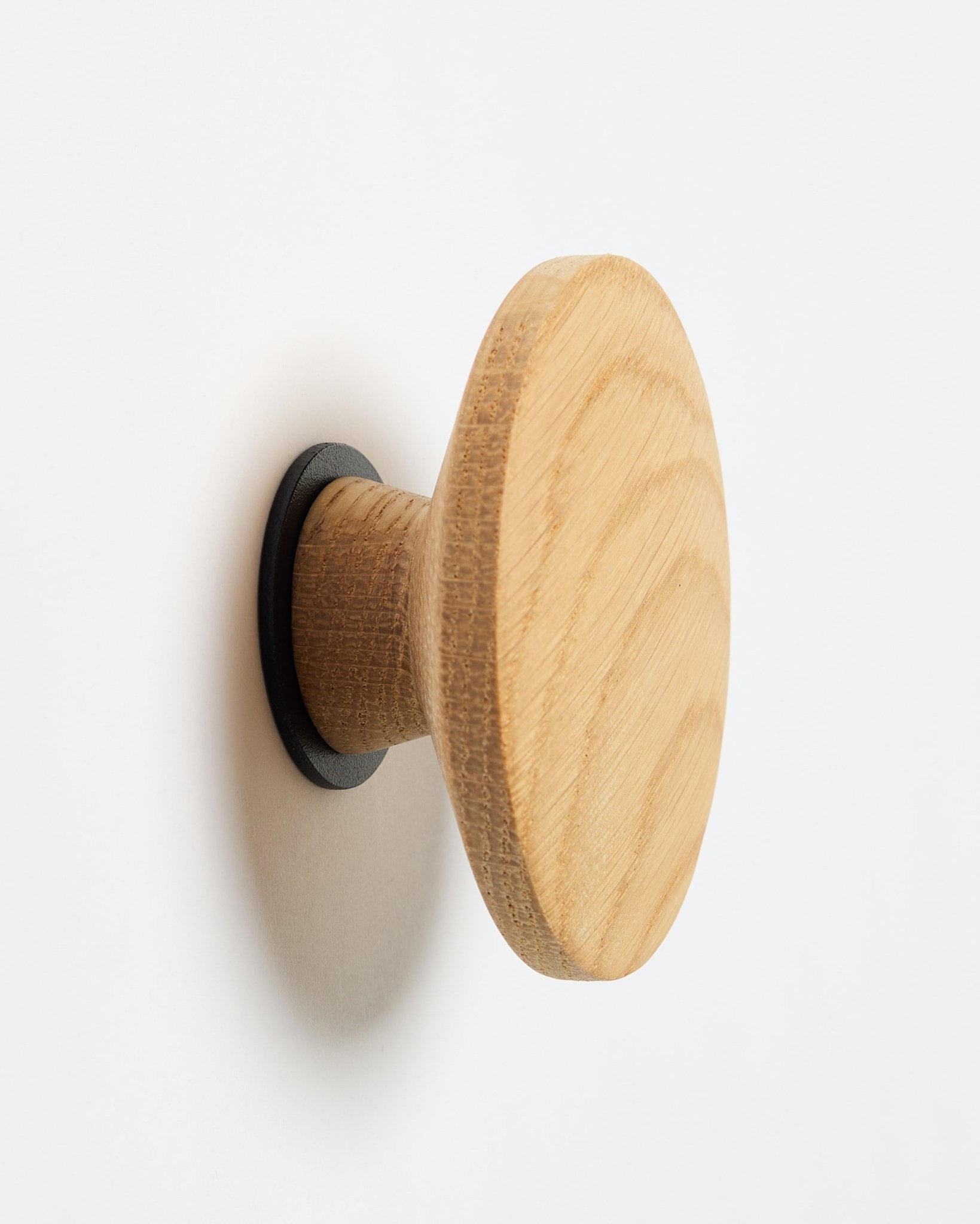 WoodUpp Linn I Single Hanger i natural oak, en rund veggkrok med black base, designet som tilbehør for montering på Akupanel akustikkpaneler i tre.