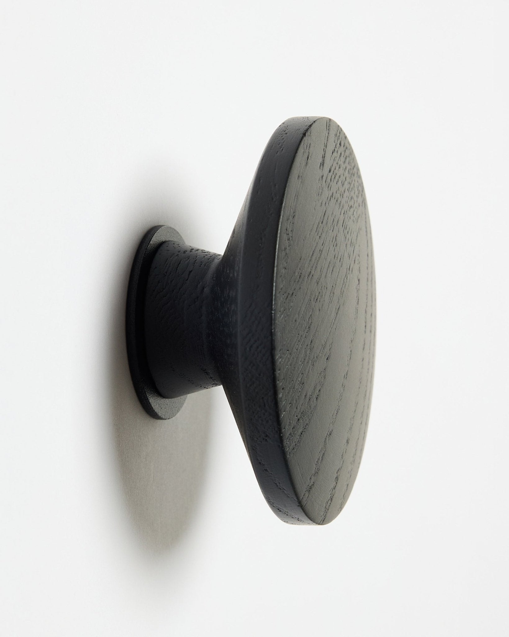 En rund Linn | Single Hanger fra WoodUpp i black oak, utformet som et tilbehør til Akupanel akustiske trepaneler, montert på en hvit overflate med en myk skygge mot venstre.