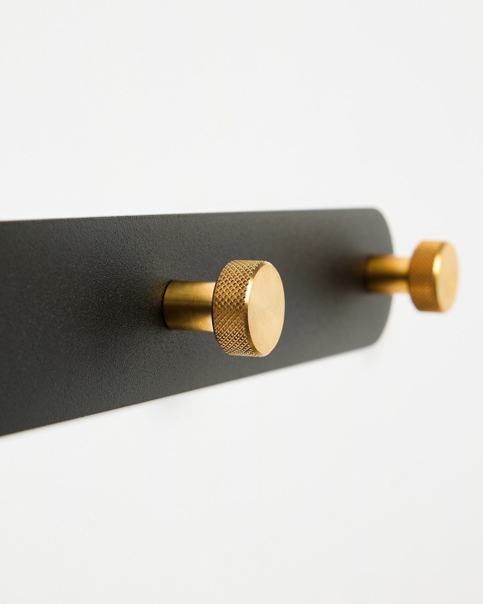 WoodUpp Norr Coat Hook Rack, modell X7, med to sylindriske black og brass kroker på et black feste, vist mot en hvit bakgrunn.