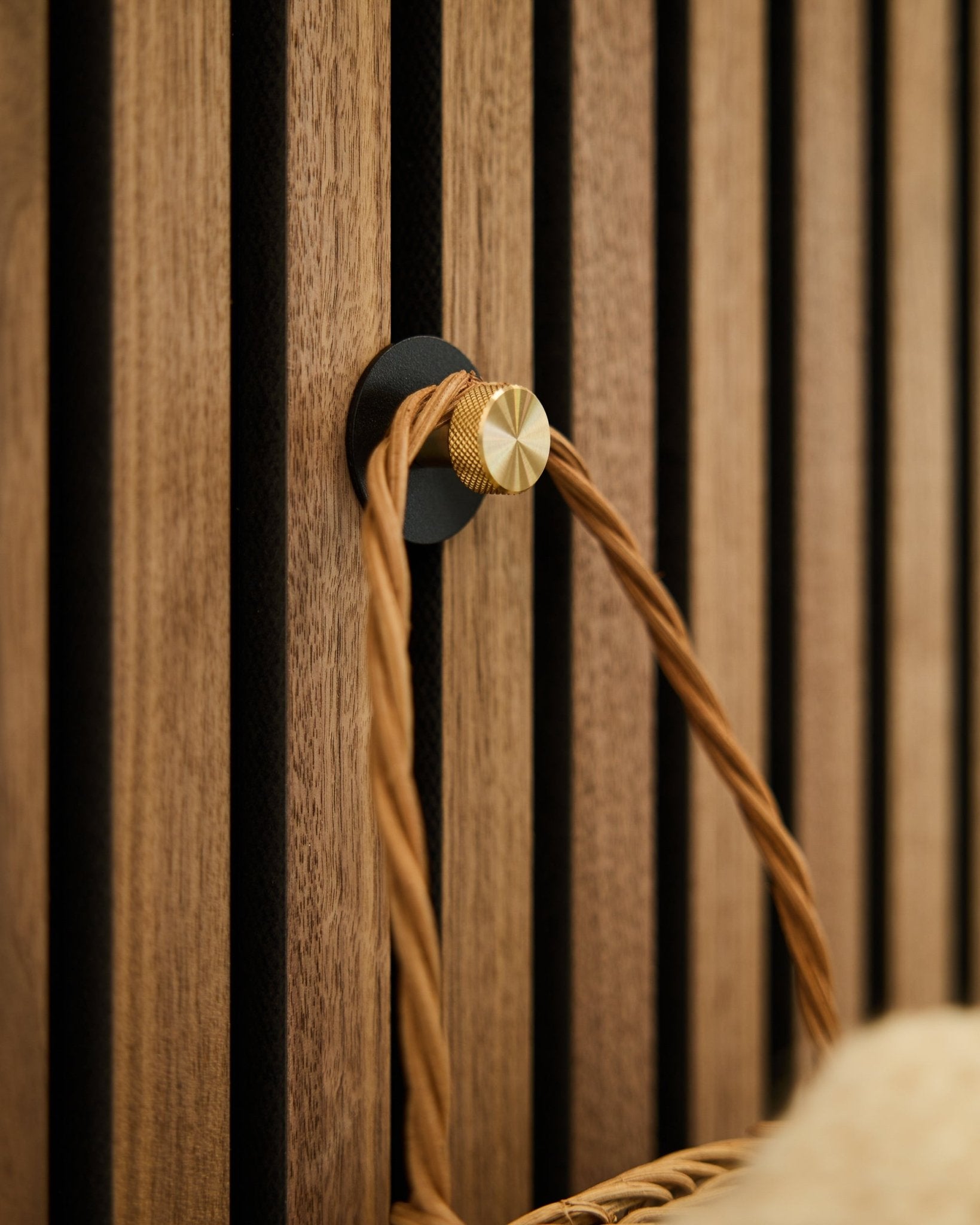 WoodUpp Norr knagg i black og brass, montert på en Akupanel Akustikkpanel i tre, holder et flettet håndtak i tan-farge.
