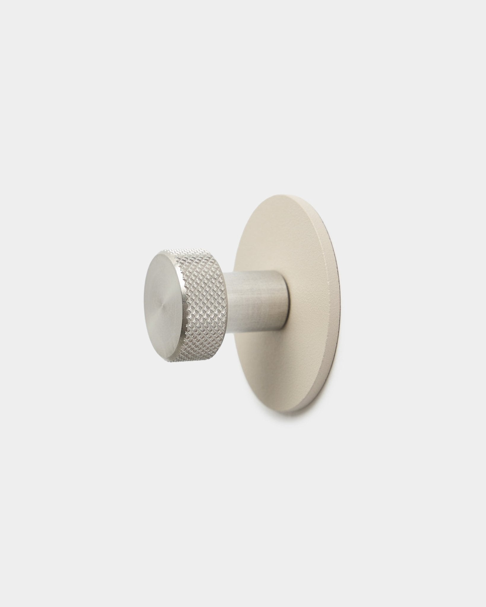 WoodUpp Norr knagg i beige og rustfritt steel med en teksturert sylindrisk ende og rund base, tilbehør til Akupanel, på en enkel hvit bakgrunn.