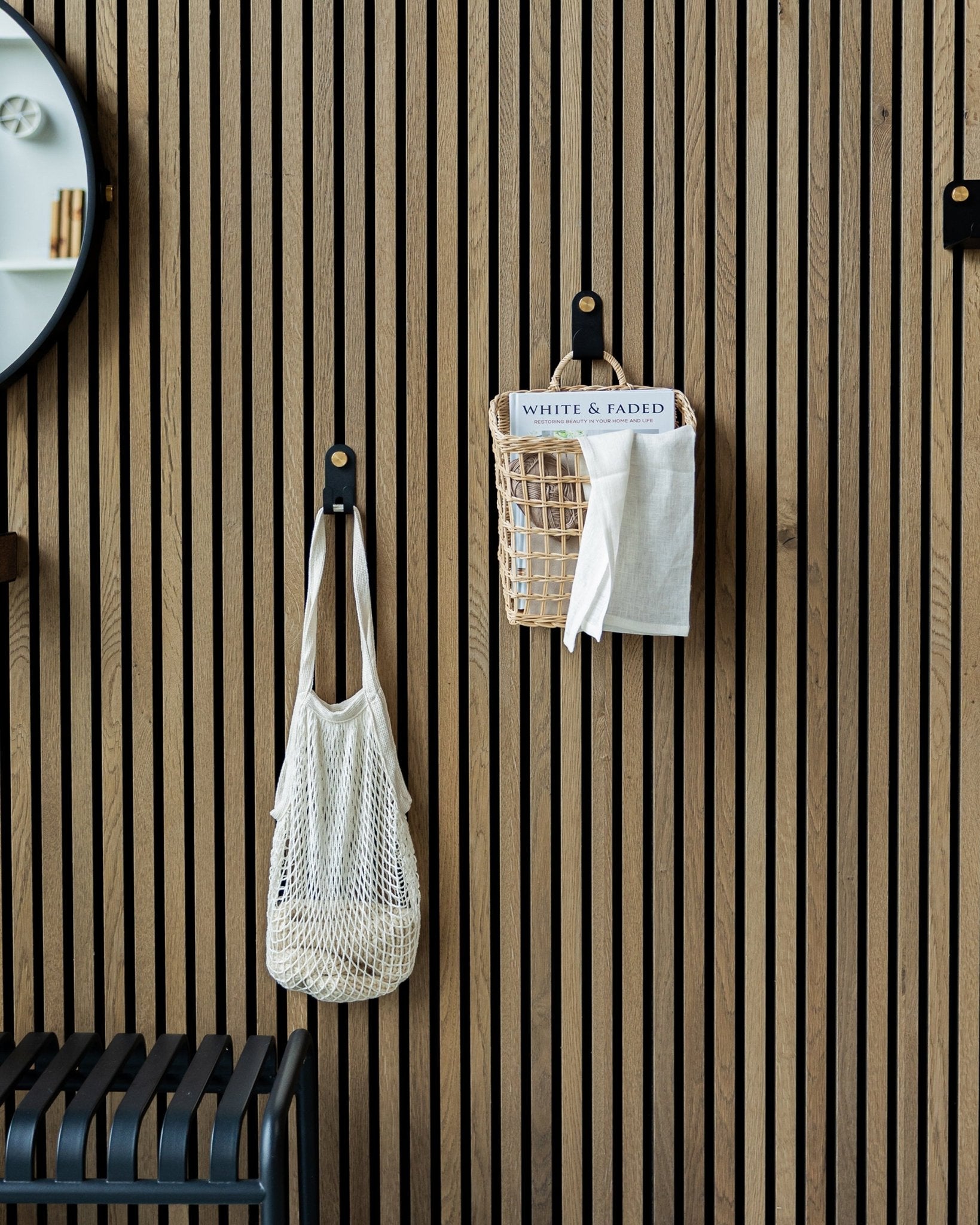 En nettingveske og en kurv henger fra Norr Single Hangers fra WoodUpp på et nordisk Akupanel Akustikkpanel i tre; en del av et speil er synlig til venstre.