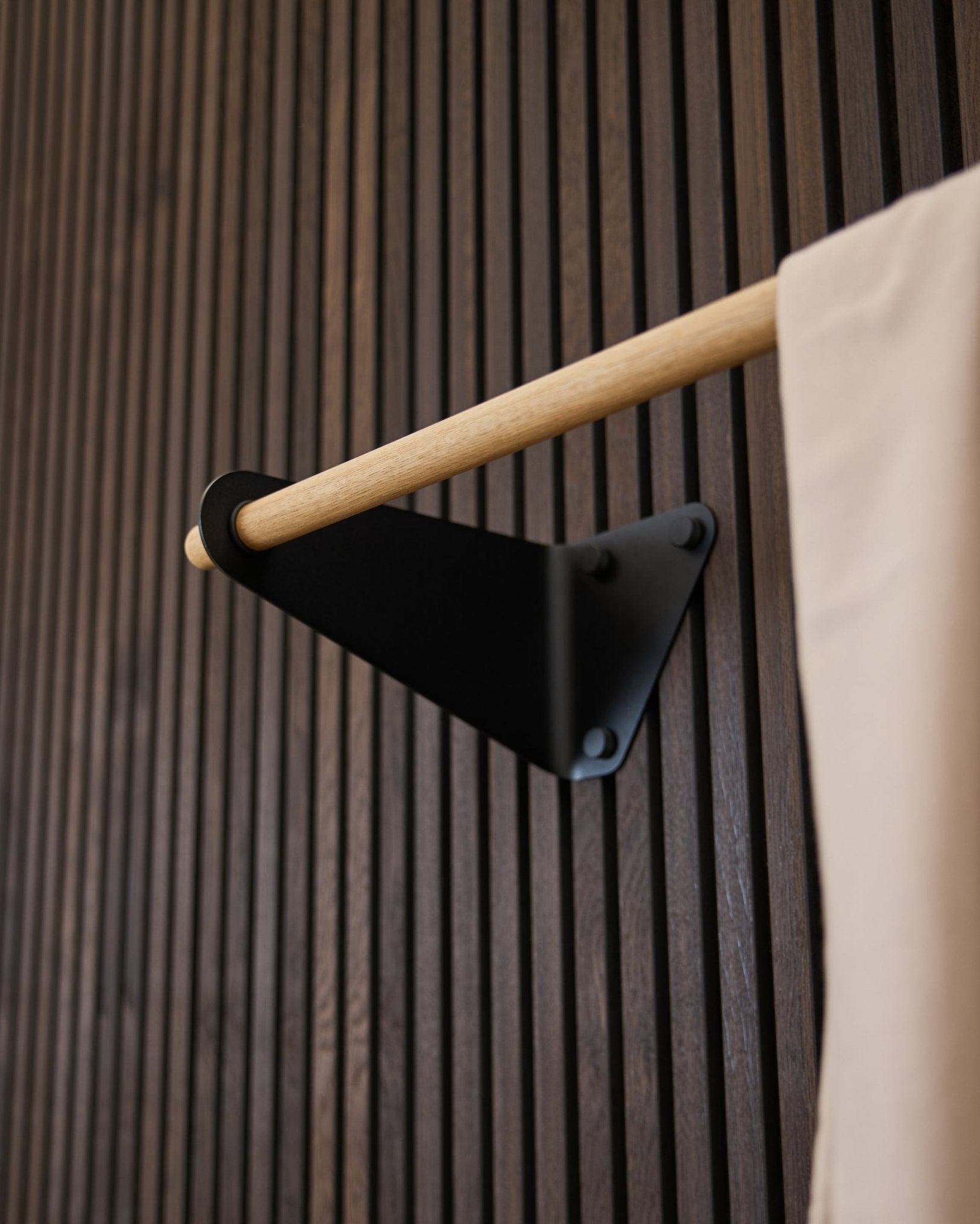 Linn knaggrekke fra WoodUpp i black (115,9 cm), montert på et mørkt rillet Akupanel Akustikkpanel, med beige stoffdetalj og black brakett.