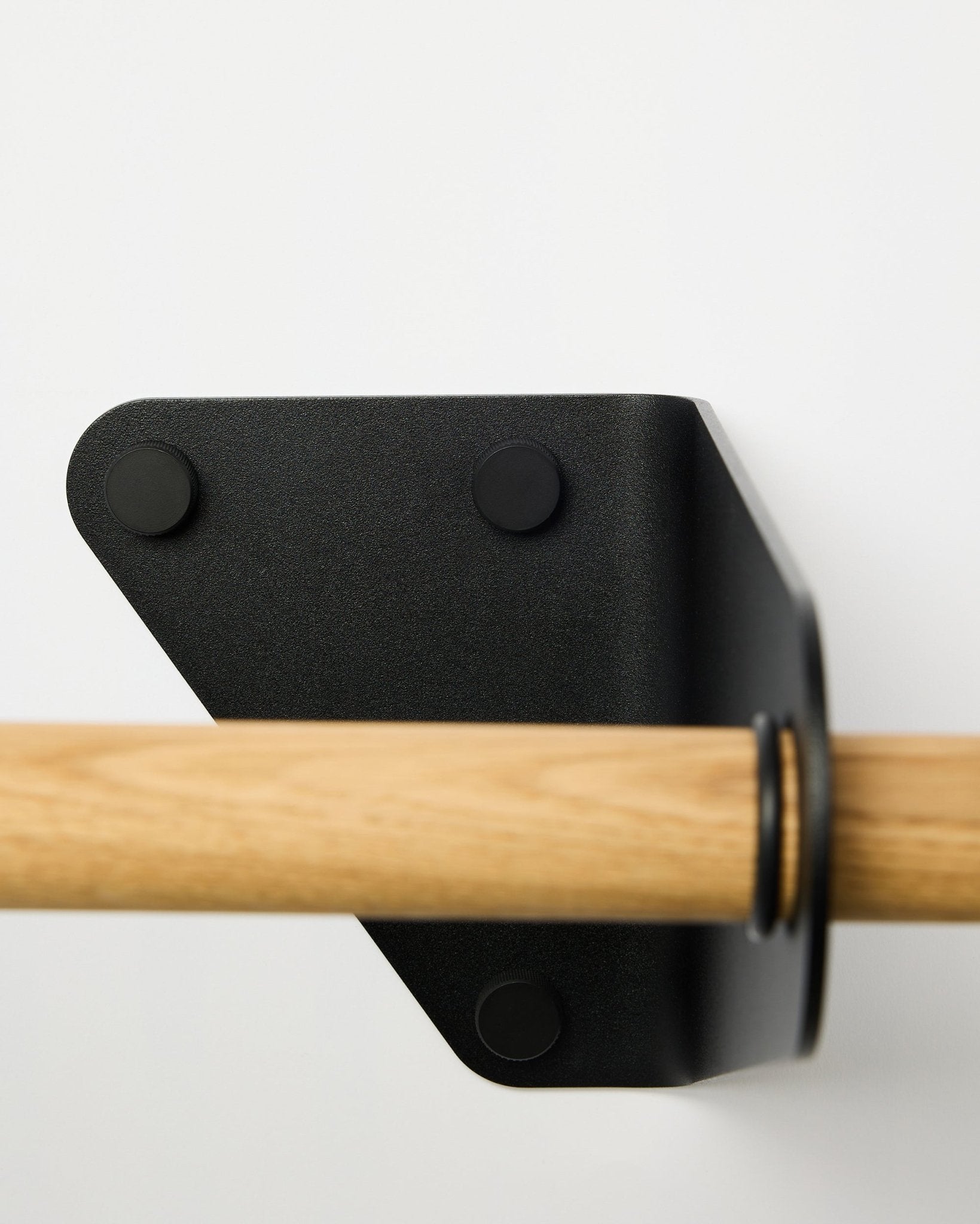 Nærbilde av WoodUpp Linn knaggrekke i black, 115,9 cm, montert på en hvit vegg med en trekantet metallbrakett, vist som en del av nordiske akustiske tilbehør.