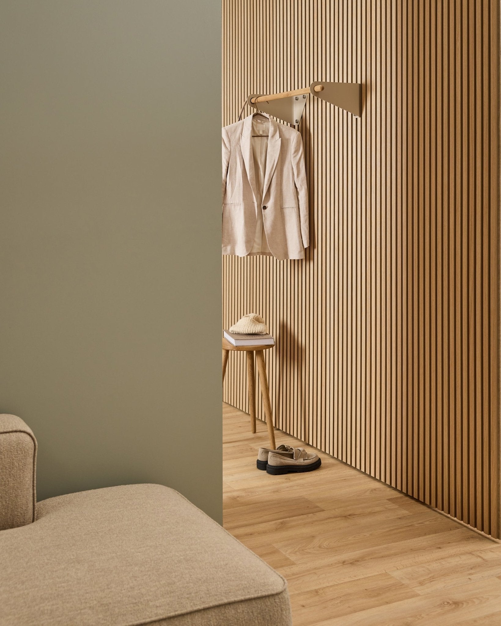 Minimalistisk rom med beige sofa, Akupanel akustisk spilevegg, WoodUpp Linn knaggrekke i beige (75,9 cm), krakk med hatt og sko på lyst tregulv.