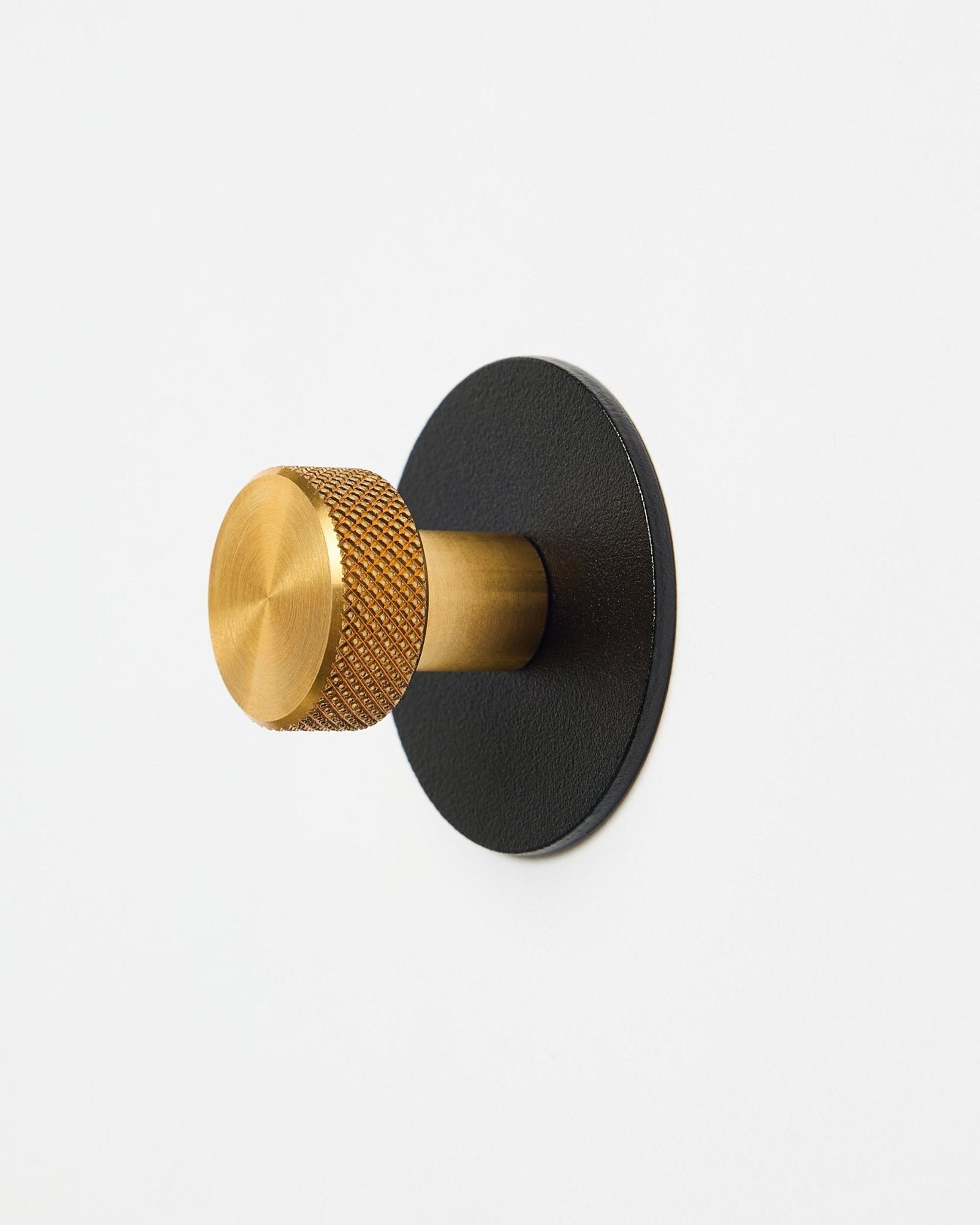 Norr Coat Hook X1 fra WoodUpp med en teksturert knott i brass og black pulverlakkert steel-base, tilbehør til Akupanel, vist på hvit bakgrunn.