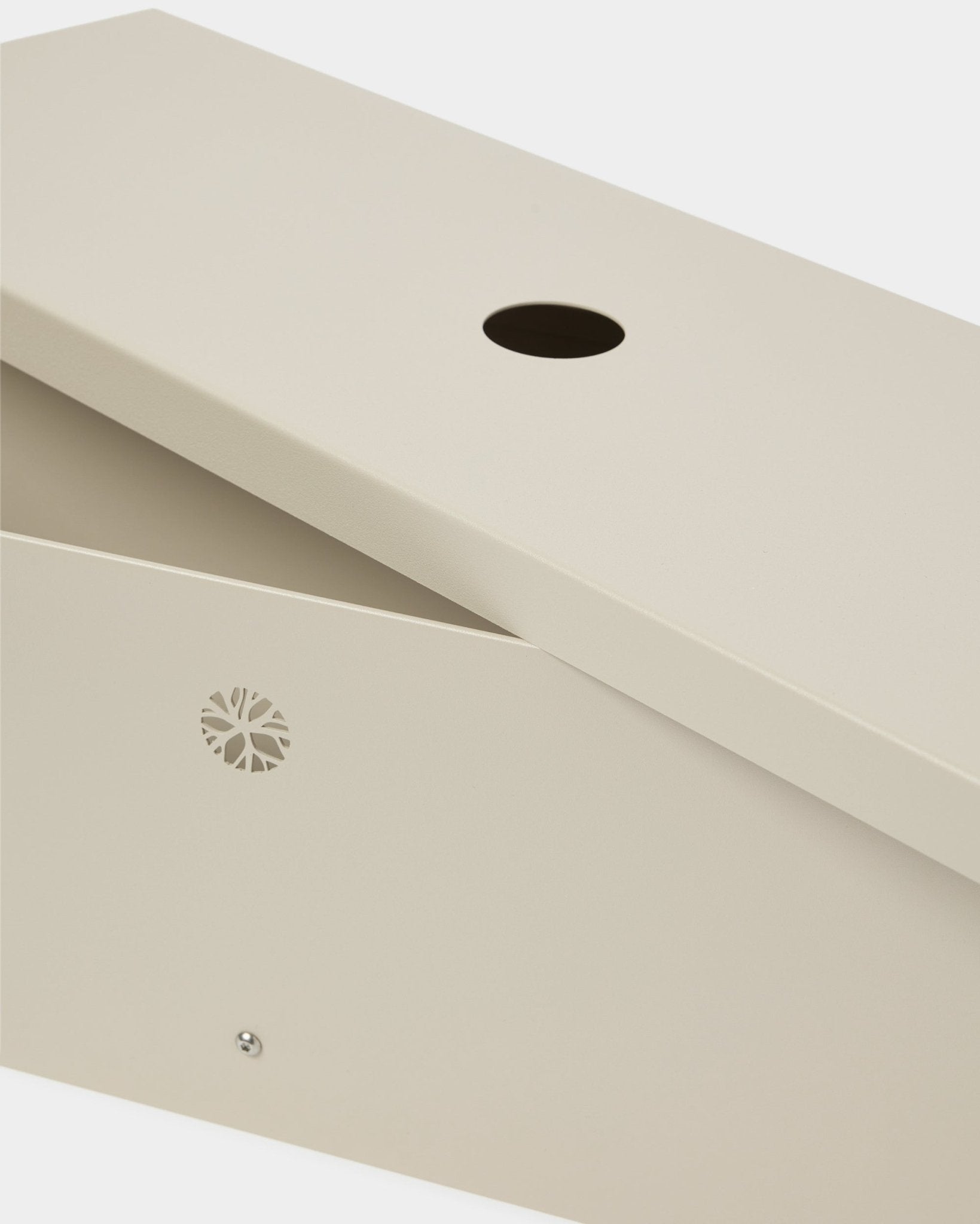 Nell | Metal Box / BM2, Beige fra WoodUpp er laget i pulverlakkert steel, med skrått lokk, sirkelformet åpning og et diskret emblem på siden.