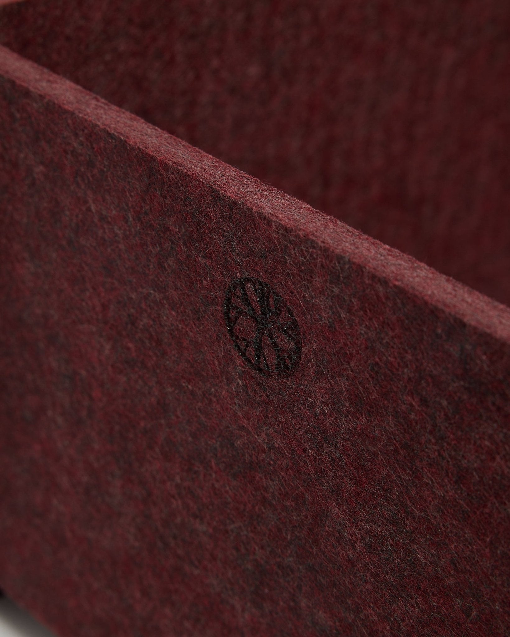 Nærbilde av WoodUpp Vigg | Felt Box / BM2 i ox red, som viser strukturert PET-filt og et sirkulært black-emblem i hjørnet. Nordisk design av akustisk tilbehør.