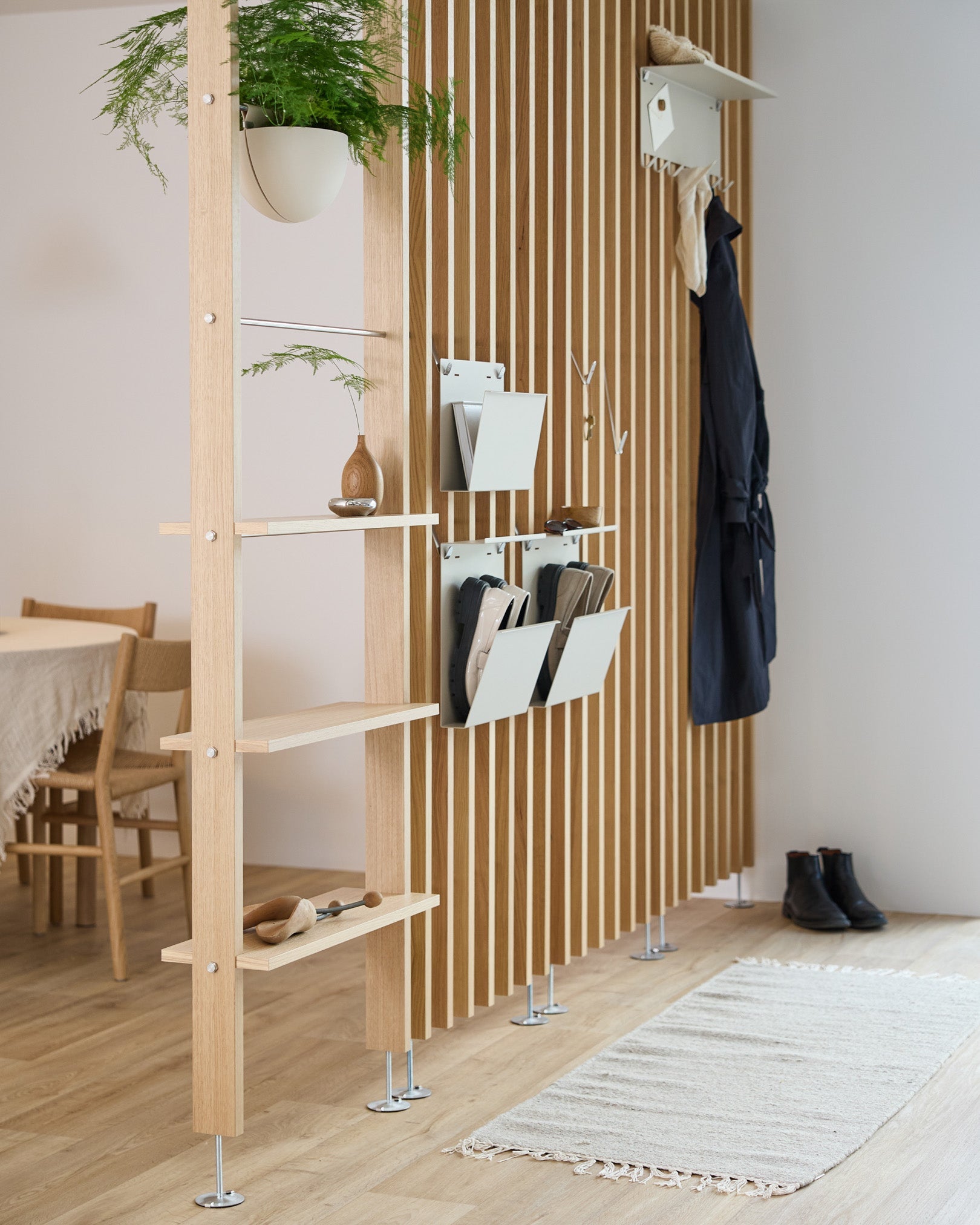 WoodUpp Nell Magazine Storage i beige integrert i en romdeler med hyller i steel, oppbevaringsbokser og knagger; spiseplass og teppe er synlige i bakgrunnen.