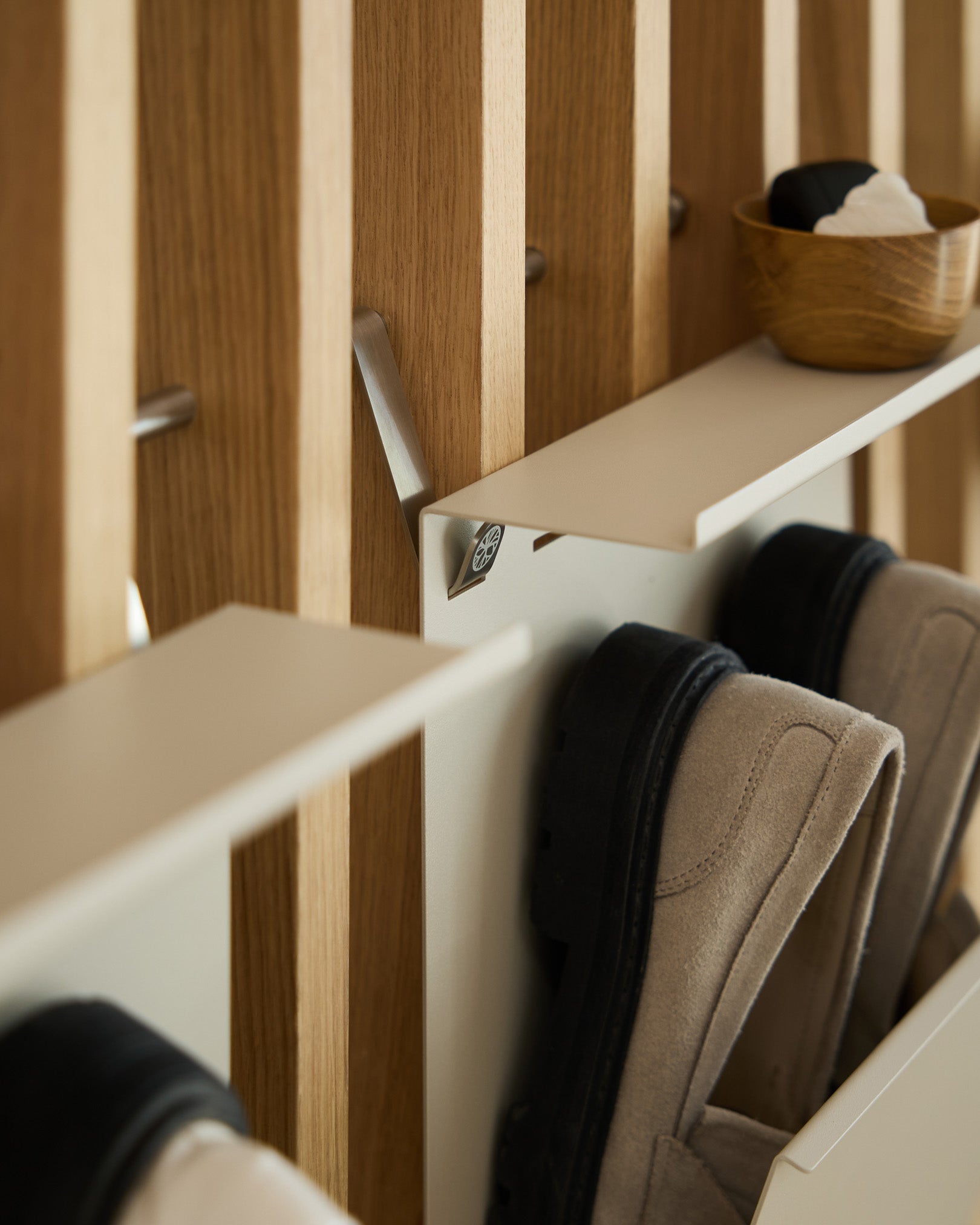 Minimalistisk beige pulverlakkert steel skohylle fra WoodUpp montert på en nordisk spilevegg Akustikkpanel, med en small skål til nøkler plassert over.