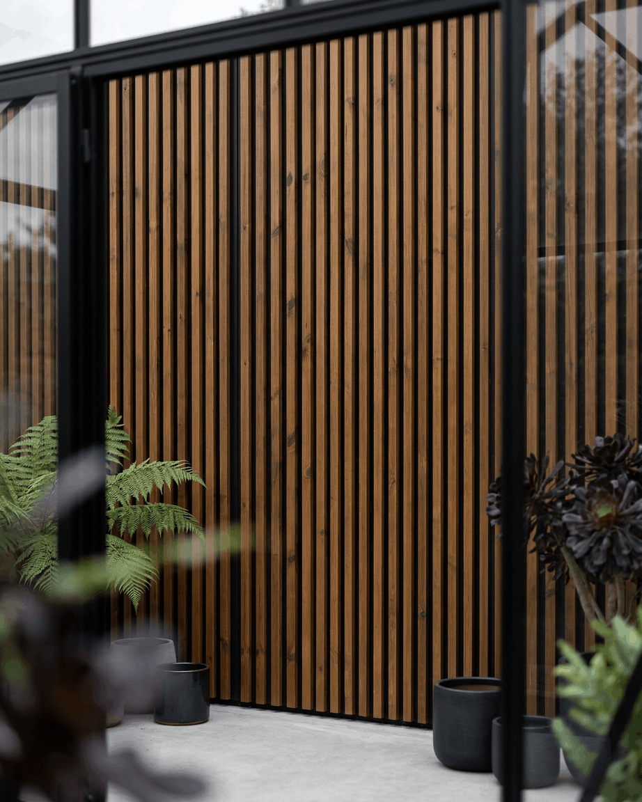 WoodUpp Aluwood utendørs fasadepanel i oljet brown kombinert med black plantekasser og grønne planter, som skaper et minimalistisk nordisk uteområde.