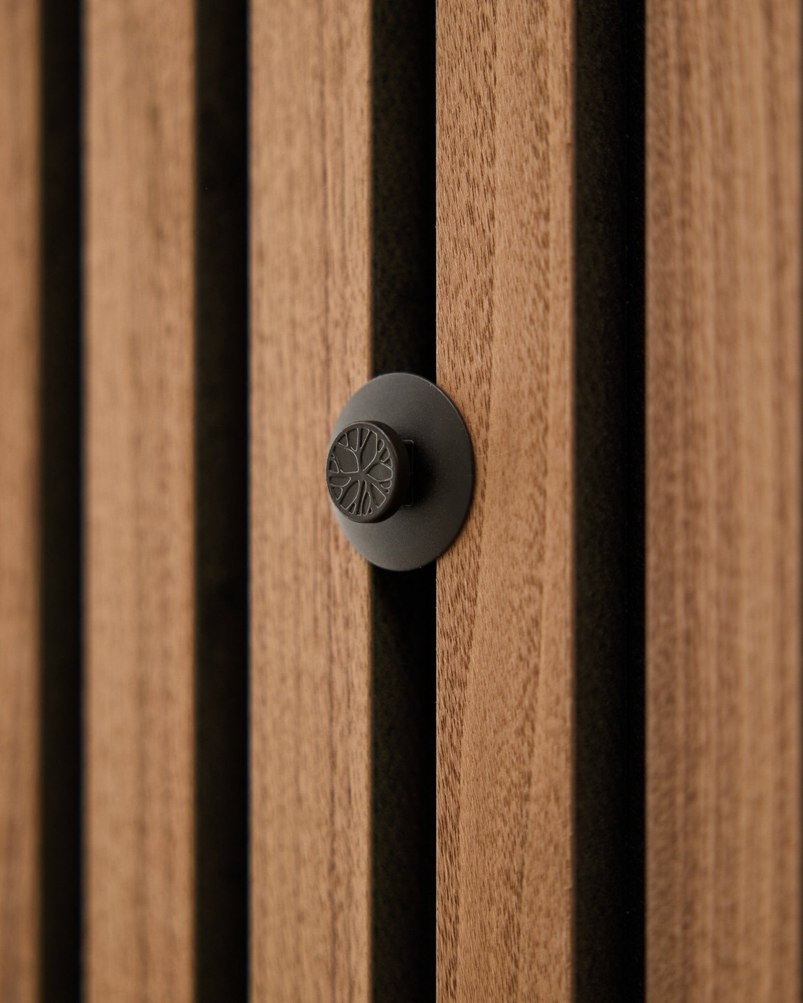 Nærbilde av en rund black-knott fra WoodUpp Dupps Original-settet, montert på en moderne vertical Akupanel akustisk spilevegg i tre.