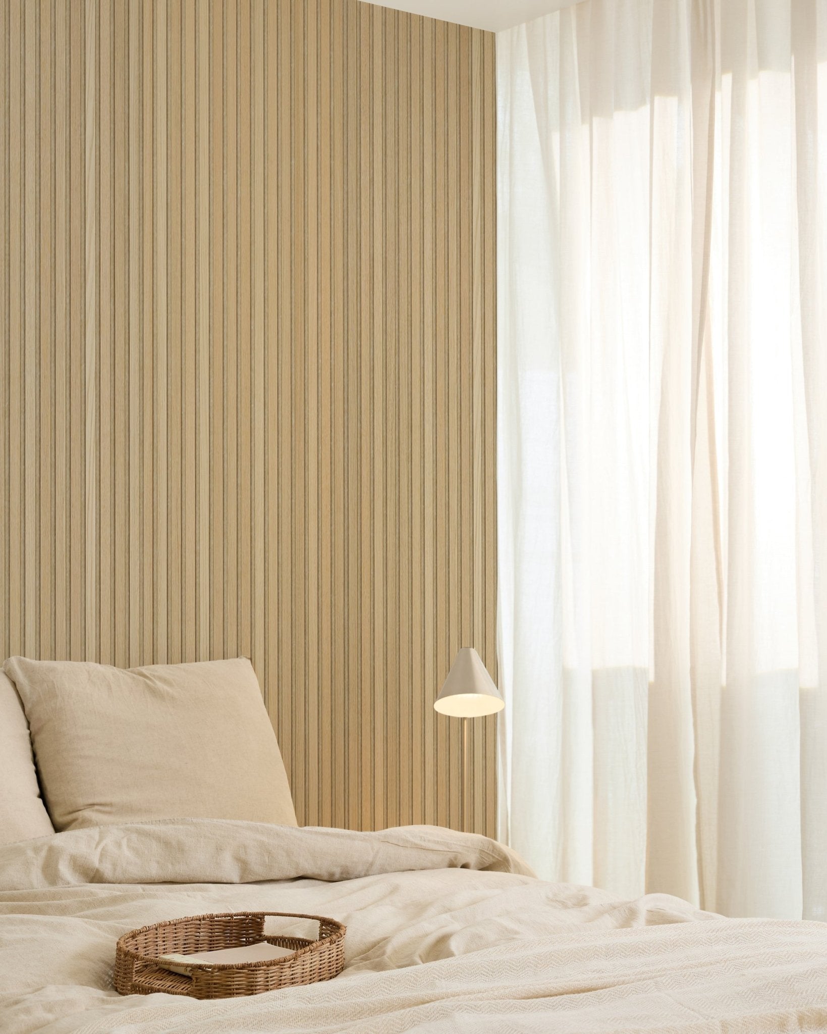 Minimalist bedroom with beige bedding, a wicker tray, modern wall lamp, Akupanel acoustic wood panel accent wall, and sheer curtains diffusing soft natural light.