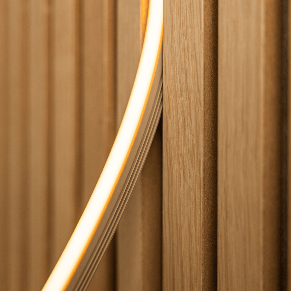 Nærbilde av WoodUpp Lumi LED-lyslist i beige (240 cm) som avgir et varmt gult lys mot Akupanel vertical akustiske trespiler; kompatibel med Philips Hue.